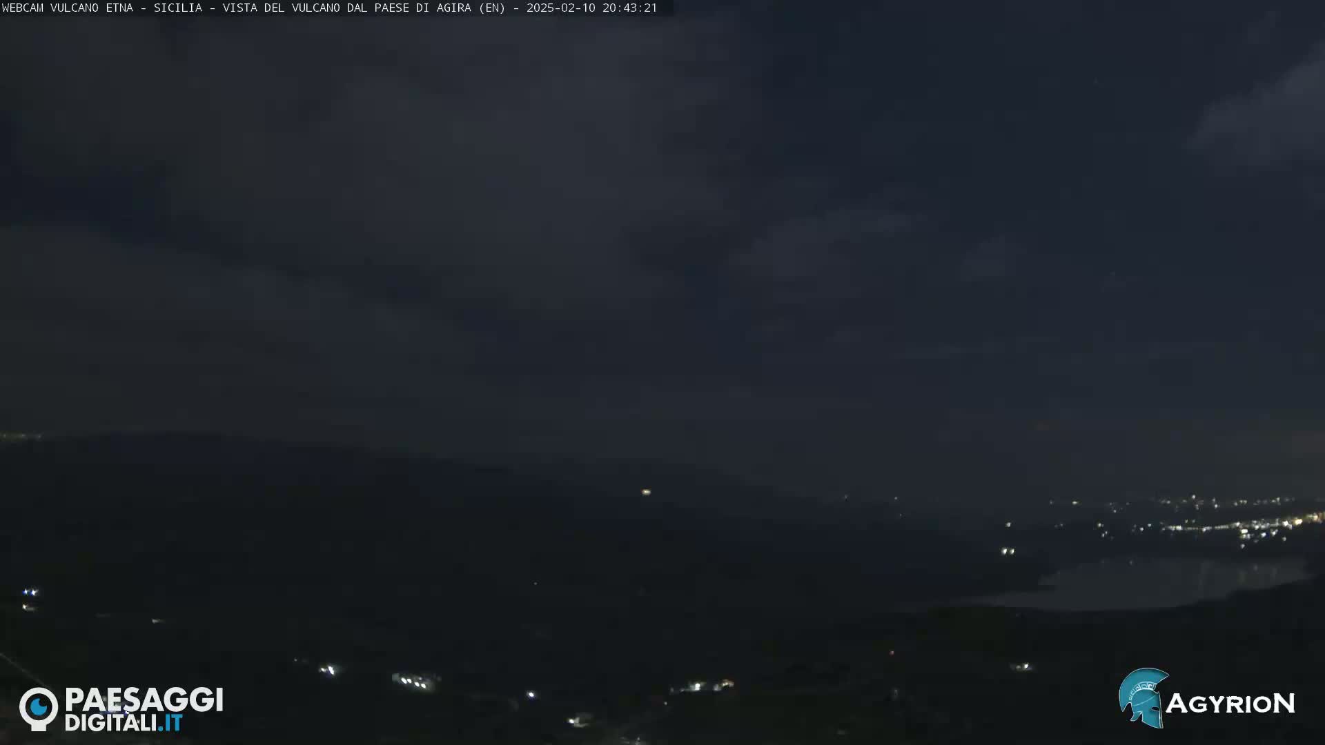 A nighttime long shot shows dark hills and a dimly lit town under a mostly cloudy sky.