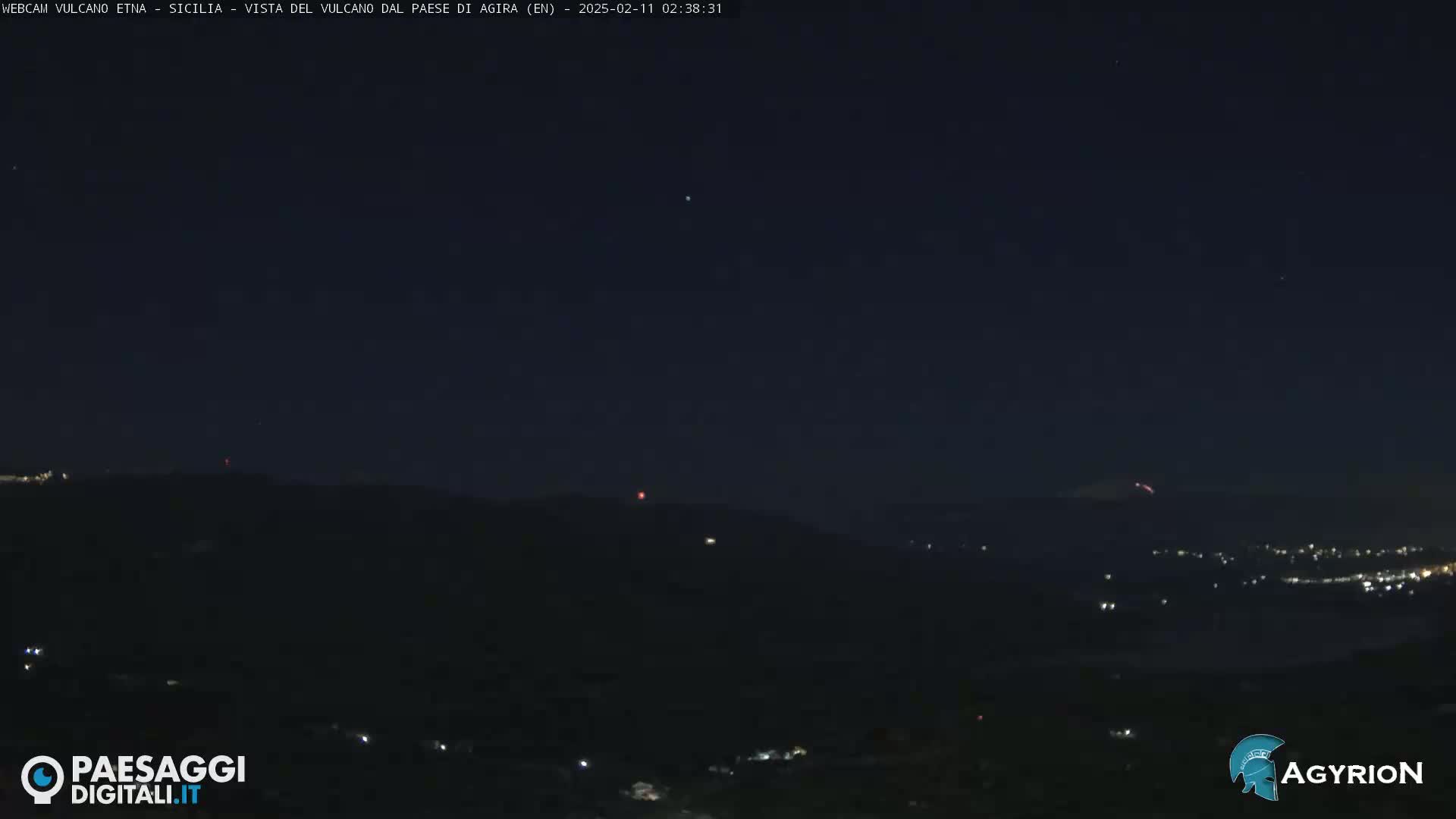 A nighttime long shot shows a dark landscape with a faint glow on the horizon, possibly from a city or town, under a clear, dark sky.