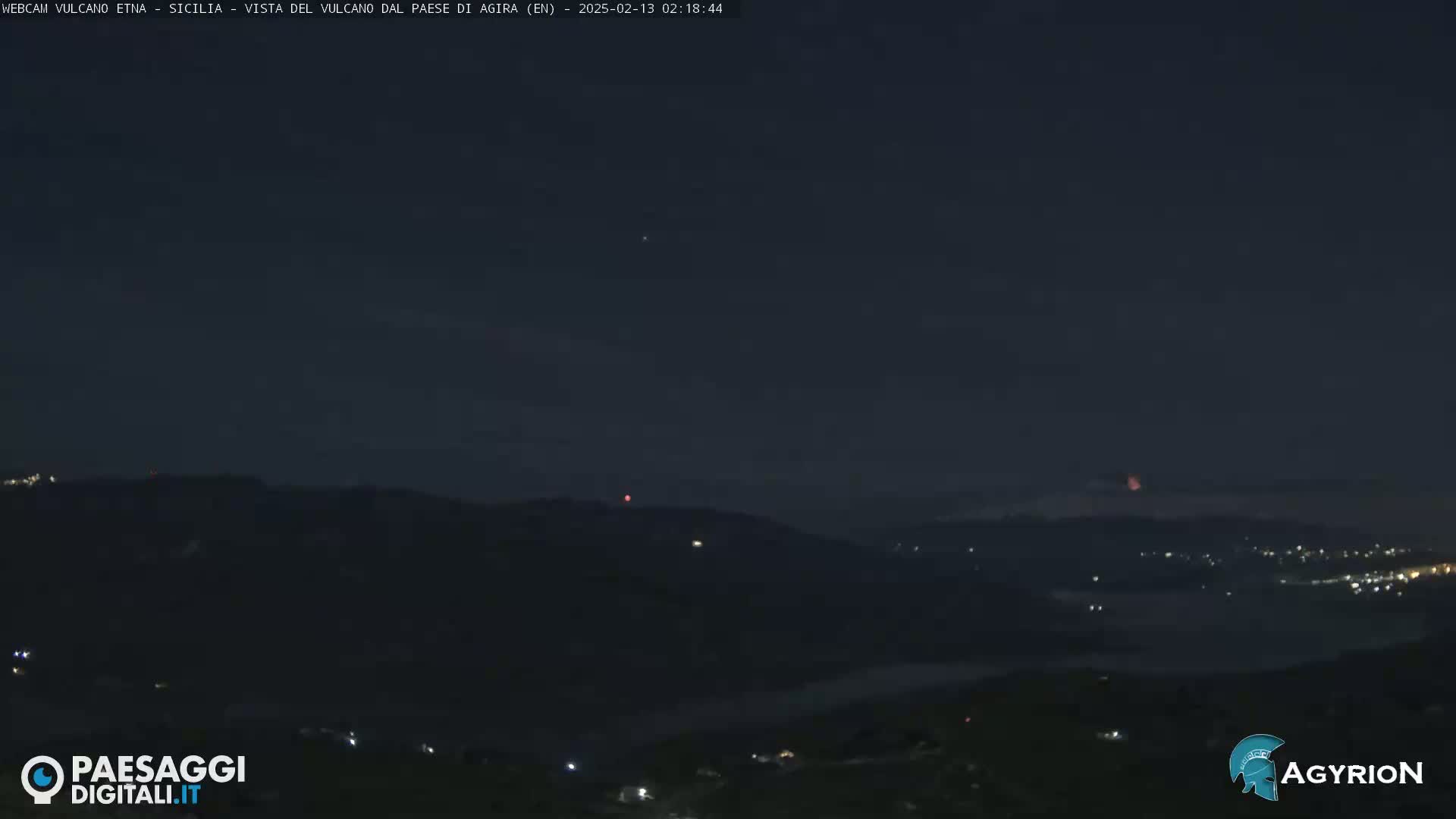 A nighttime long shot shows a dark, hilly landscape with a few scattered lights, under a mostly clear, dark sky with a faint glow on the horizon.