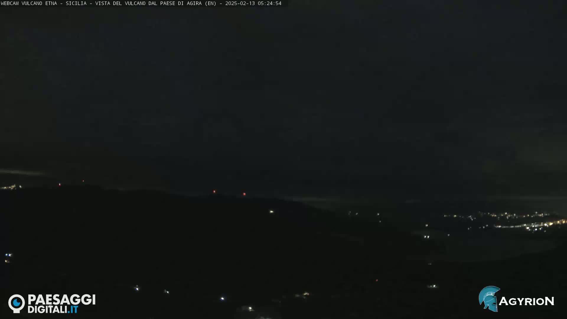 A nighttime, dark view of a distant, dimly lit town below a dark, mostly cloudless sky.