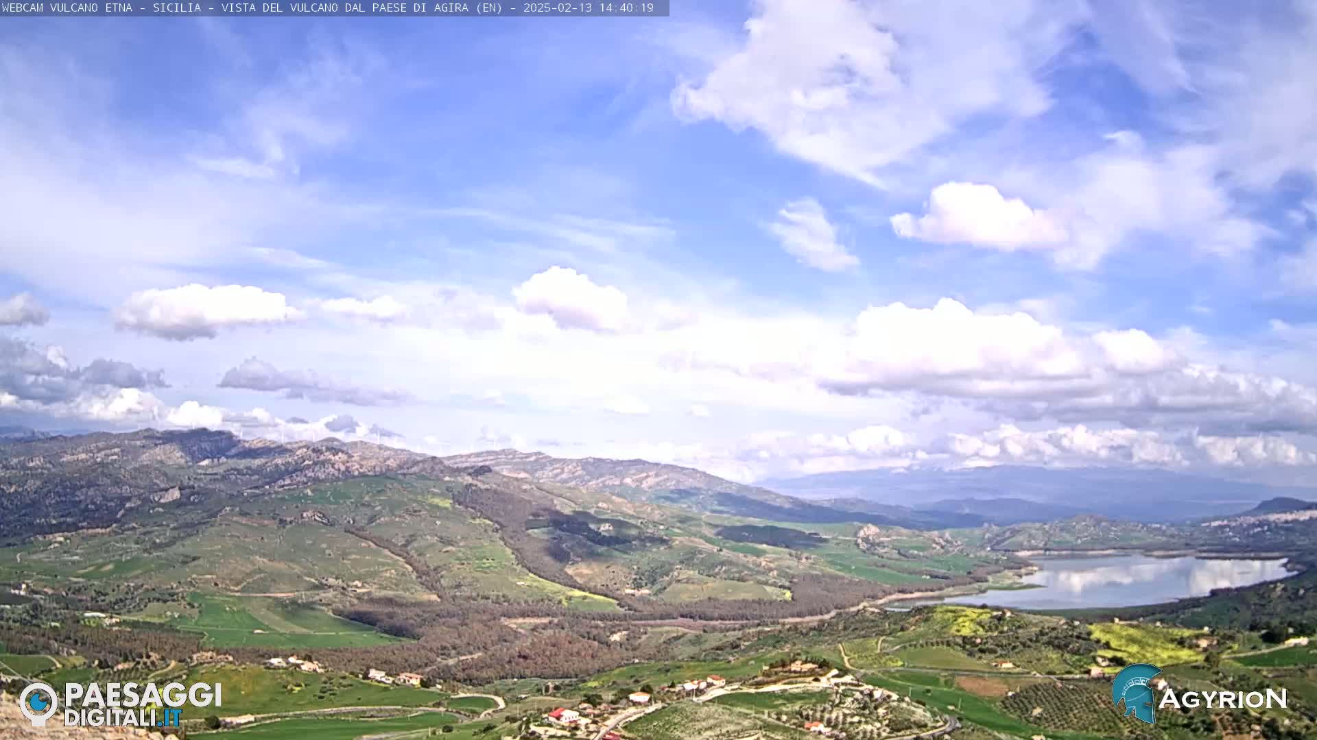 A partly cloudy sky overlooks a hilly landscape with a lake and farmland under it.