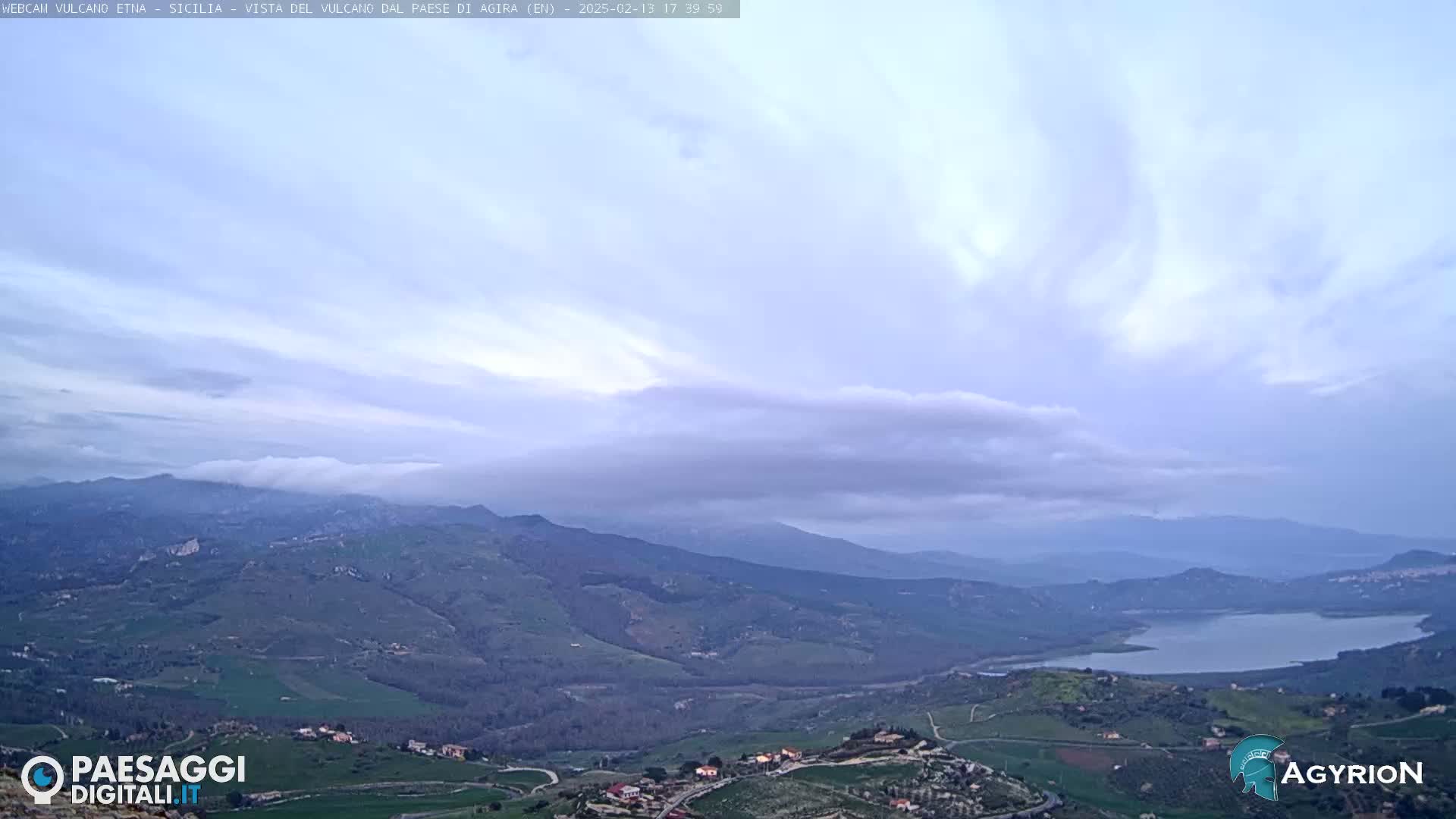 A view of rolling hills and a lake under a mostly cloudy sky.