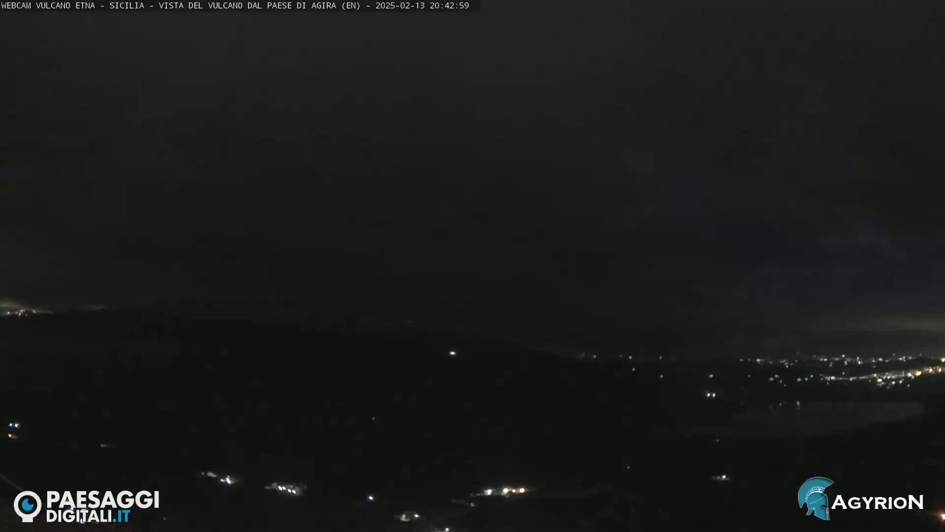 A nighttime, dark view of a distant city illuminated by lights, under a mostly clear, dark sky.
