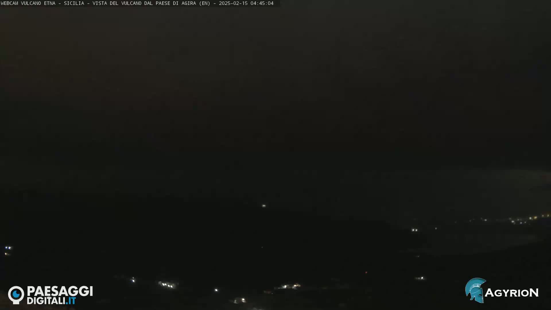 A dark, nighttime view of a landscape with a few faint lights visible in the distance.