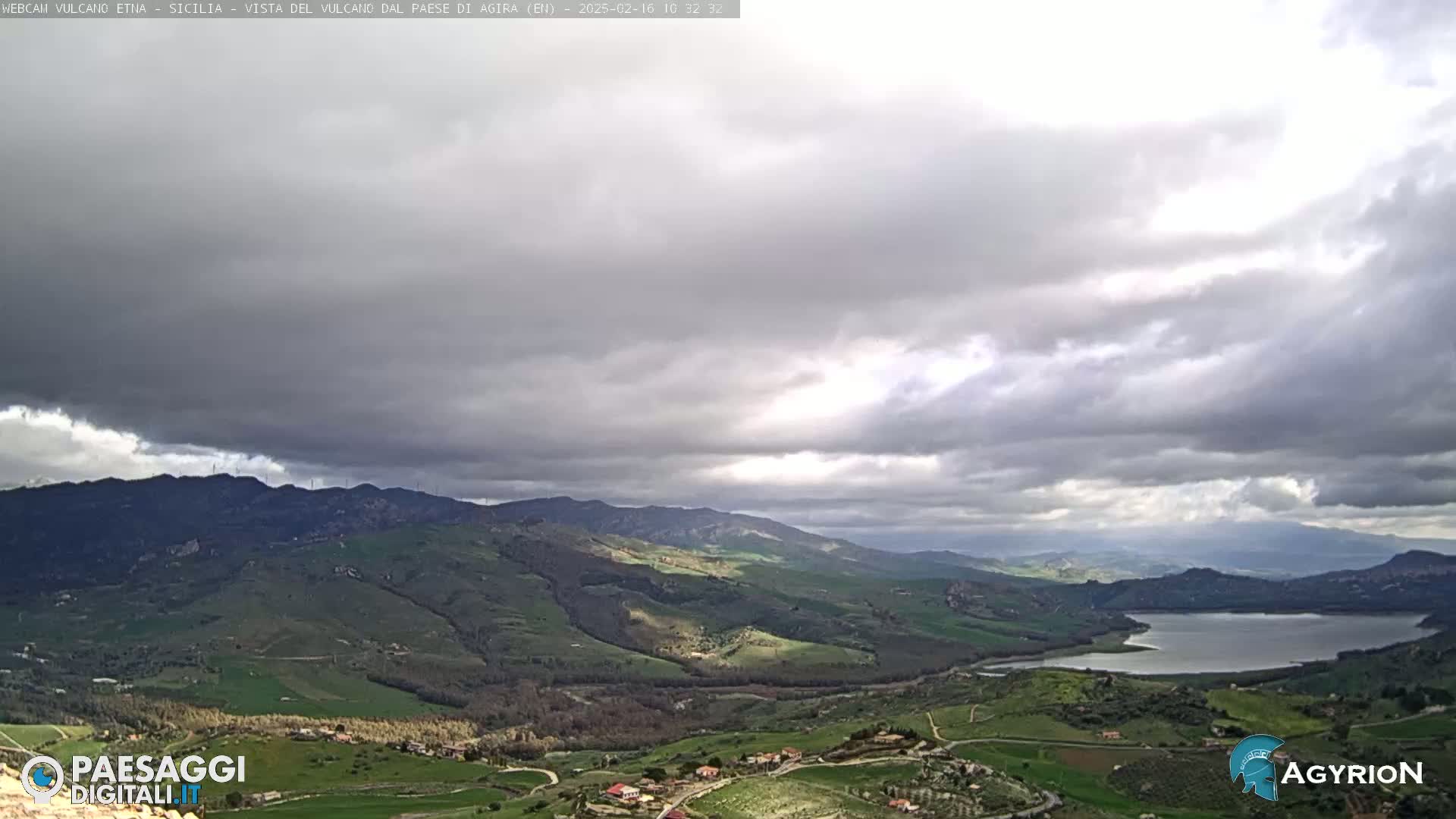 A view of a valley with rolling hills and a lake under an overcast sky.
