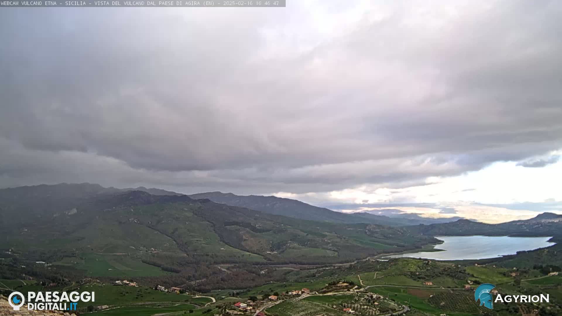 A vast, hilly landscape with a lake is visible under a mostly cloudy sky.