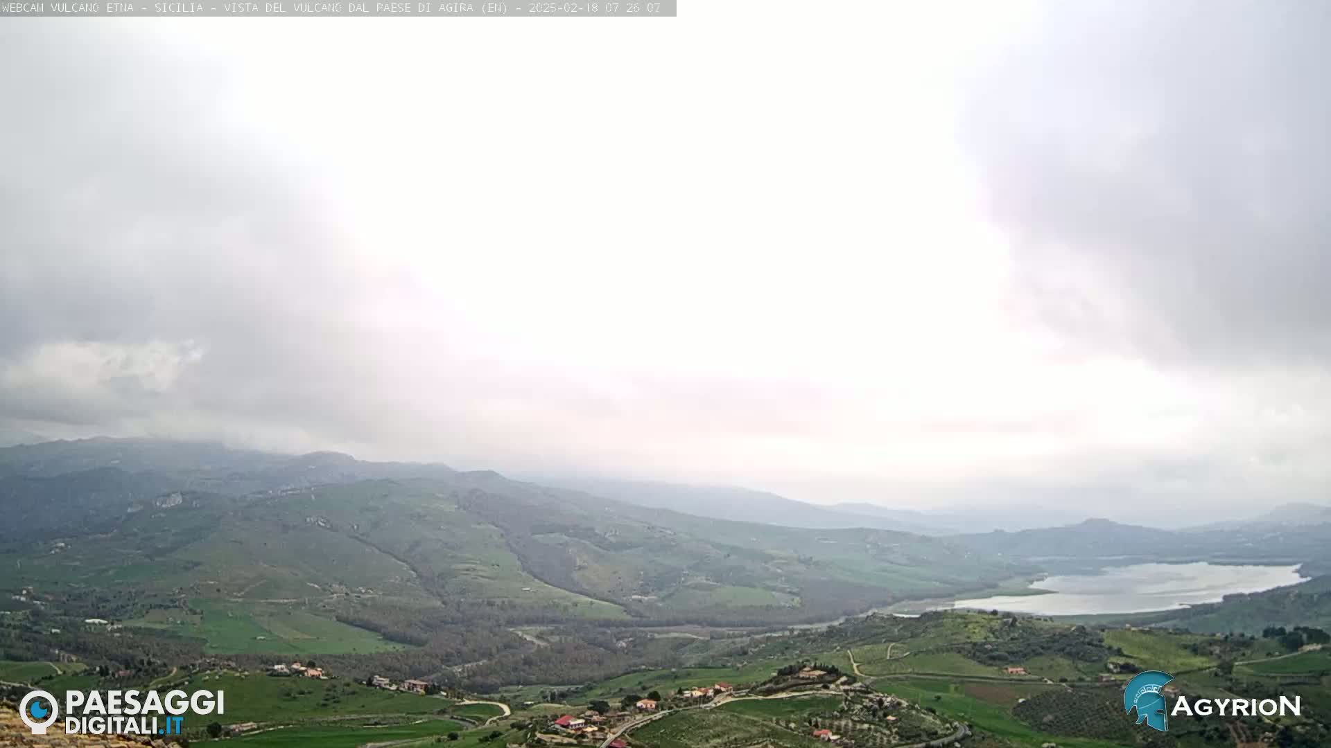 A vast, hilly landscape stretches under an overcast sky, featuring a lake in the middle distance.