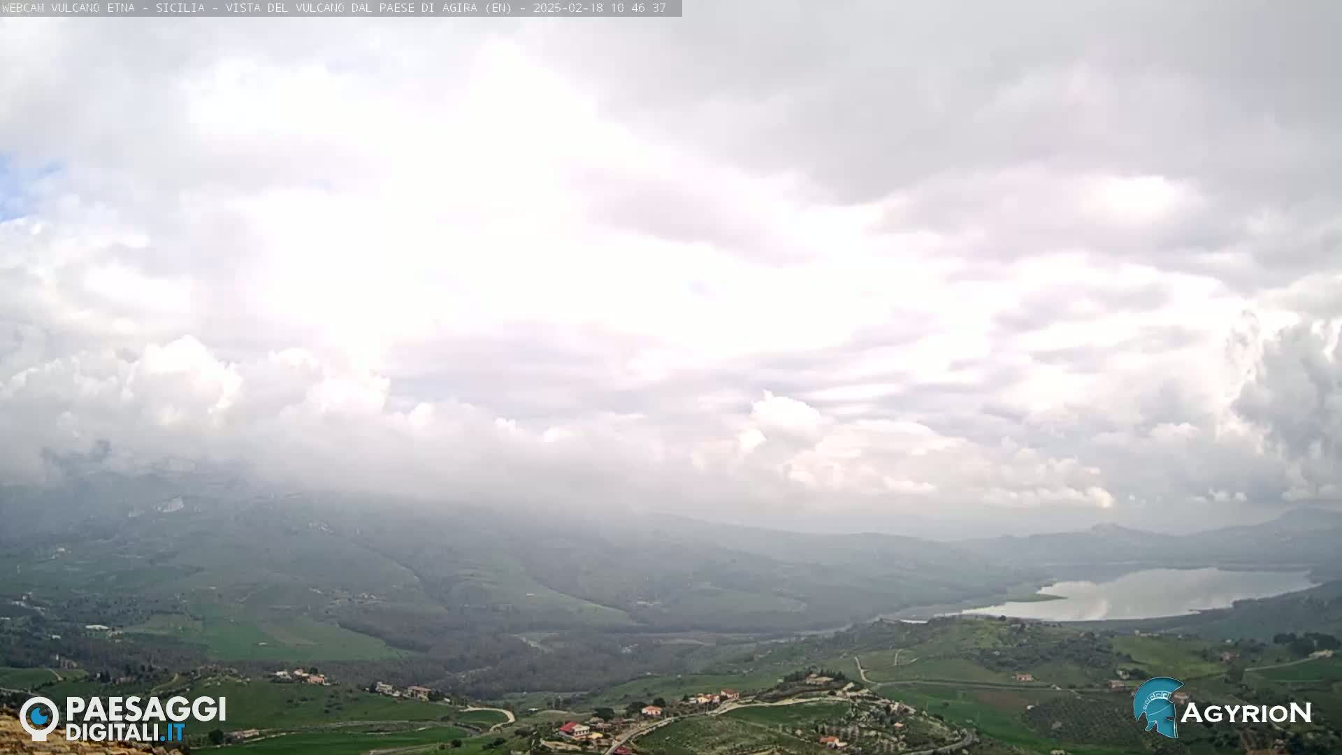 A hazy, cloudy day reveals a view of rolling green hills and a lake in the distance.