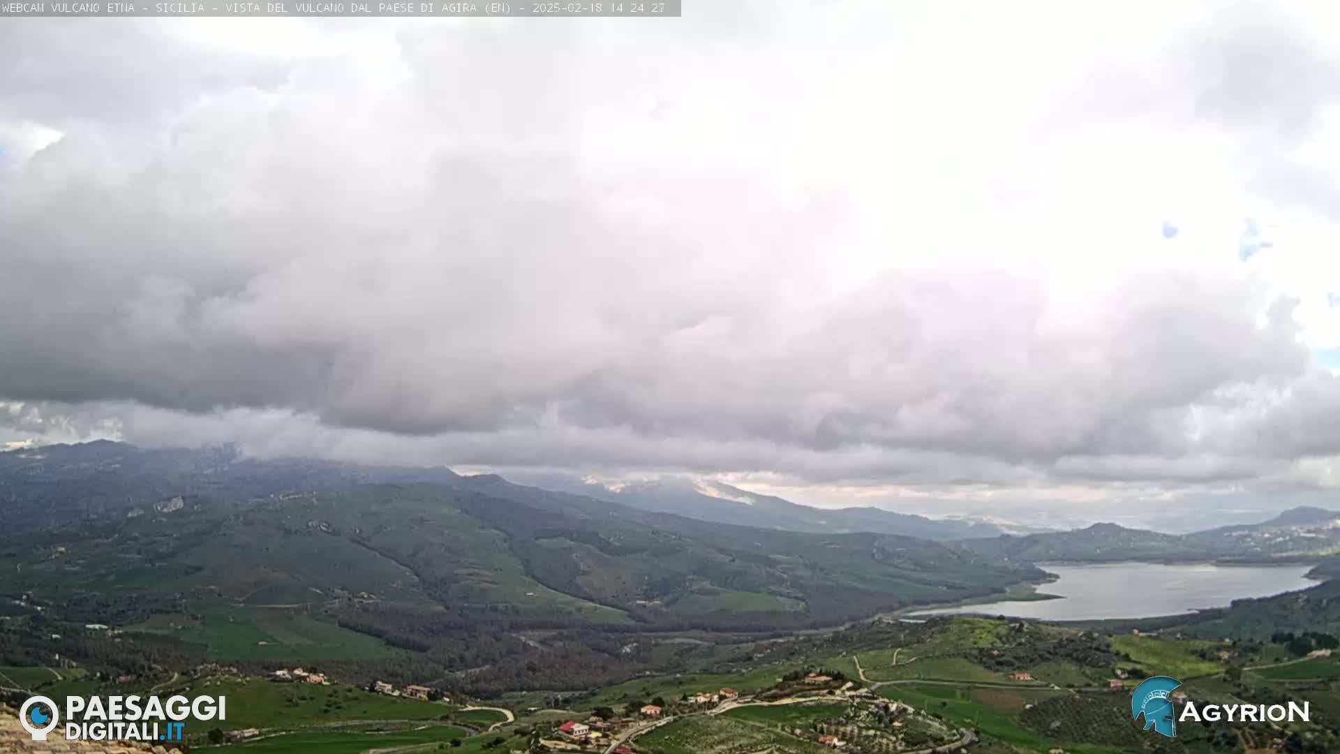 A sprawling, hilly landscape under a cloudy sky features a large lake nestled in a valley.