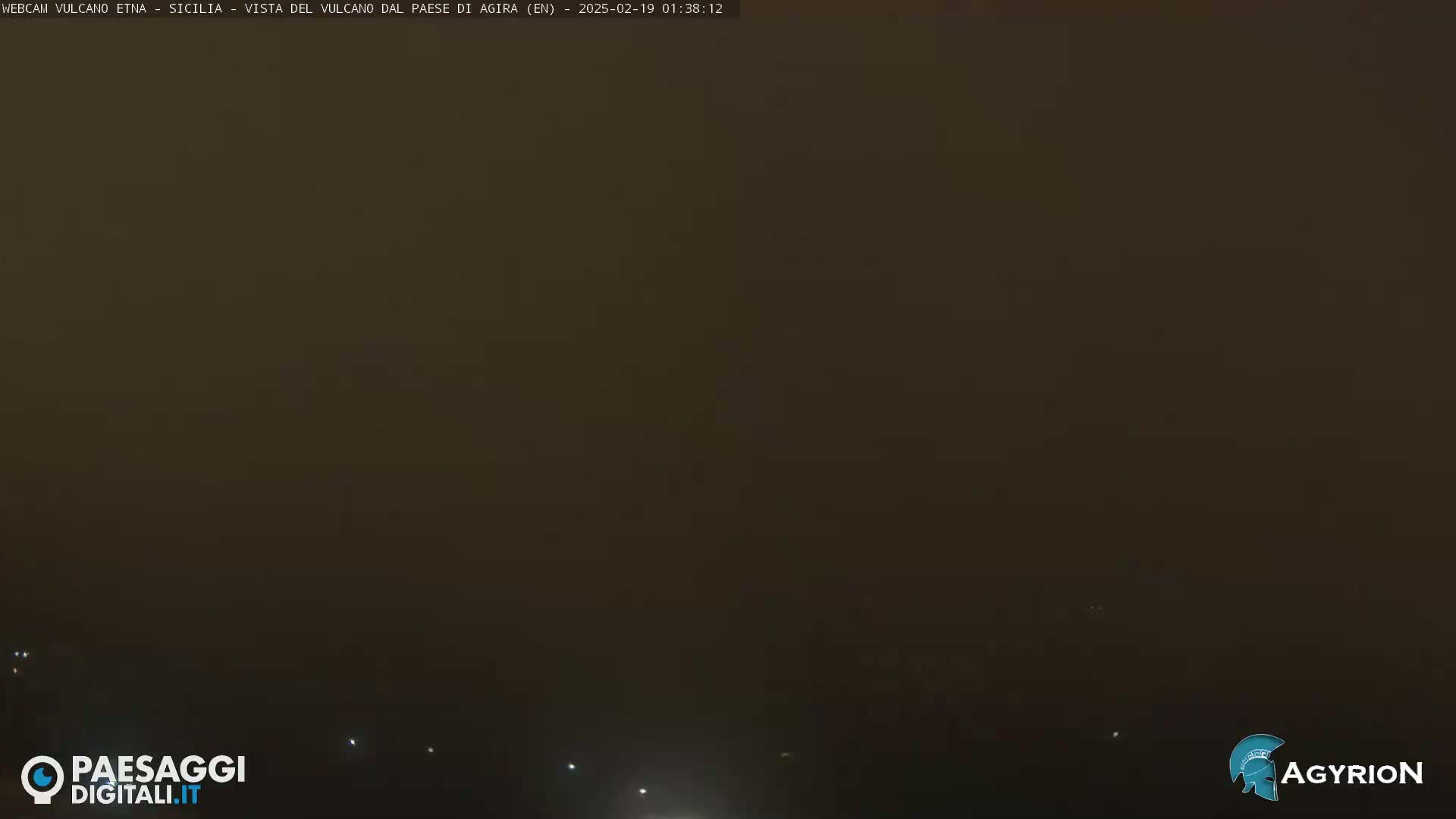 A dark, hazy, nighttime view of a landscape with a few faint lights visible in the distance.