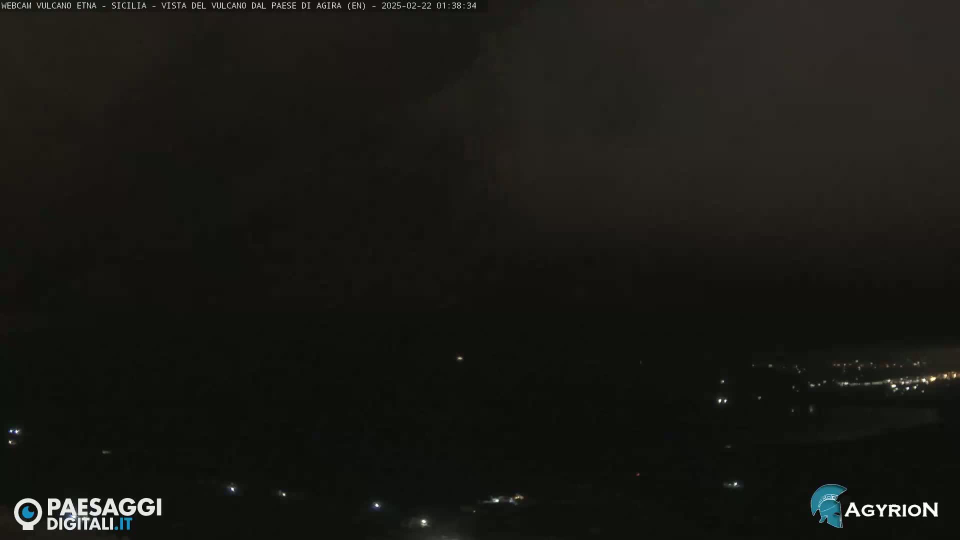 A dark, nighttime view of a dimly lit landscape, possibly a town or city, under a mostly cloudy sky.
