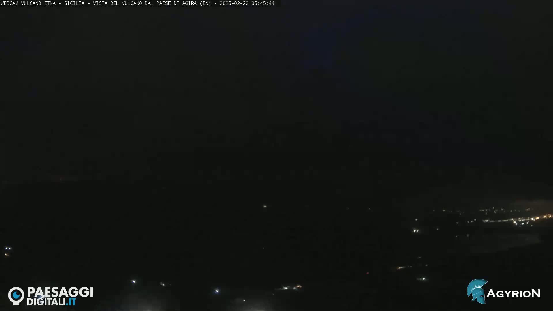 A nighttime long shot shows a dark landscape with a few scattered lights in the distance under a mostly dark sky.