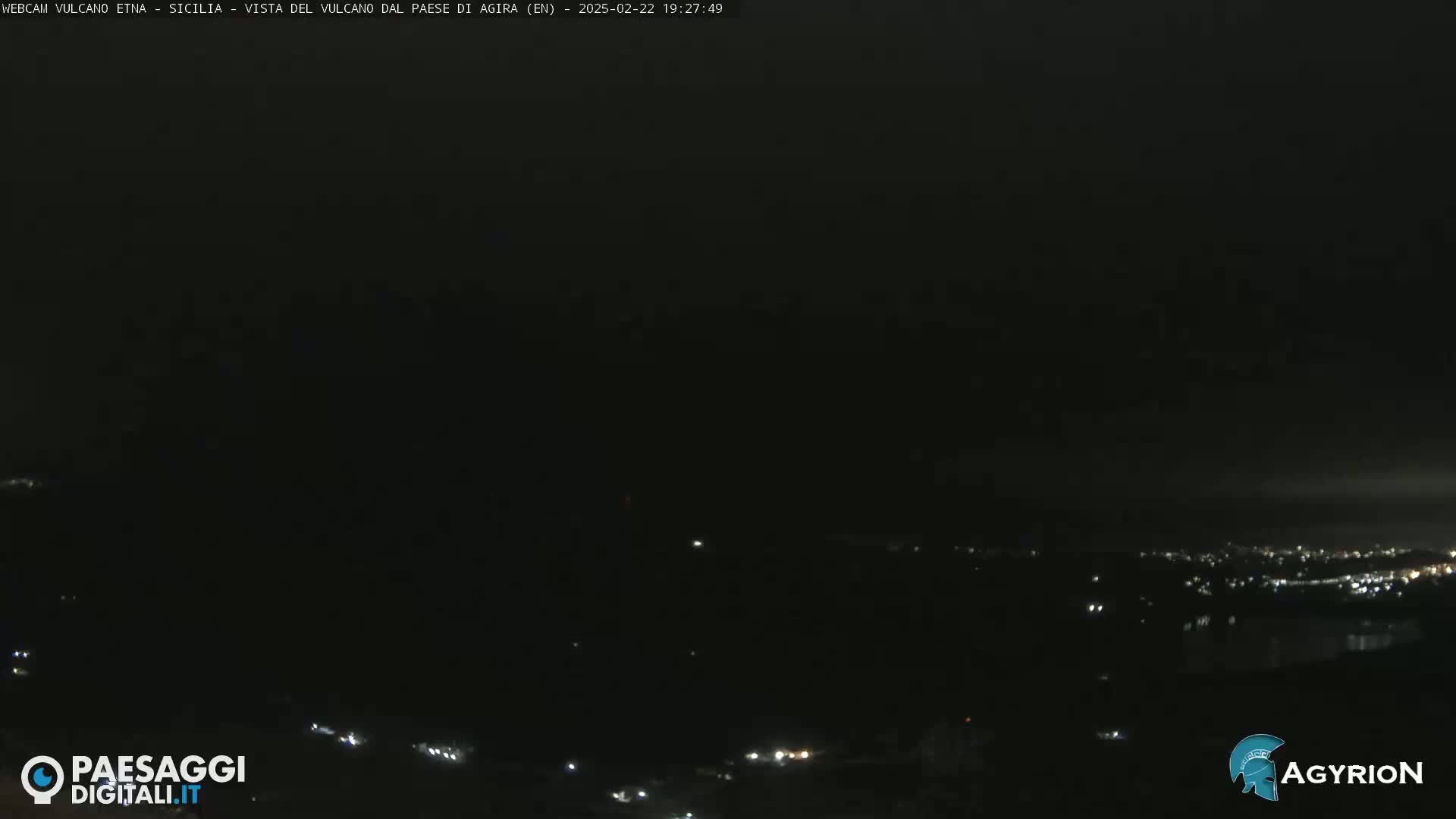 A nighttime, dark view of a distant town with scattered lights, under a mostly cloudy sky.