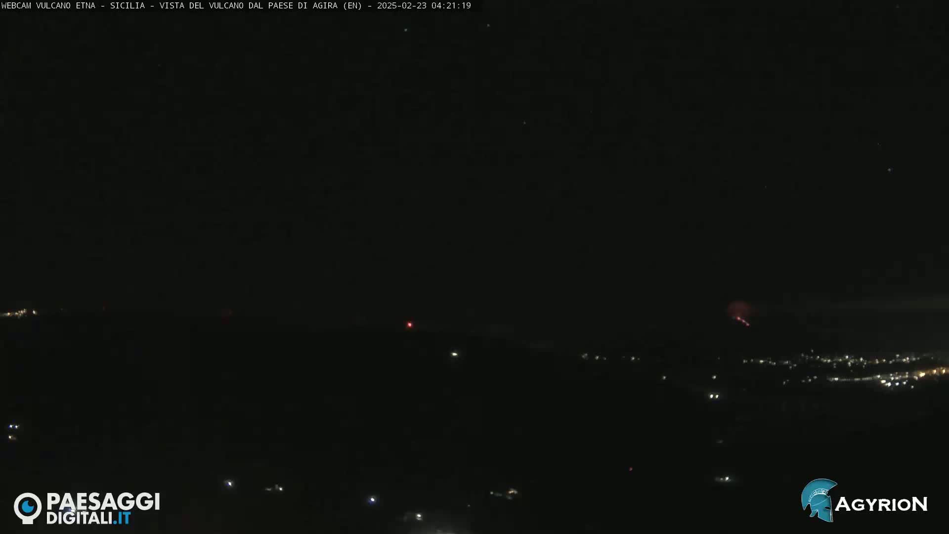 A nighttime long shot shows a dark landscape with a few scattered lights, and a faint reddish glow on the horizon under a clear, dark sky.