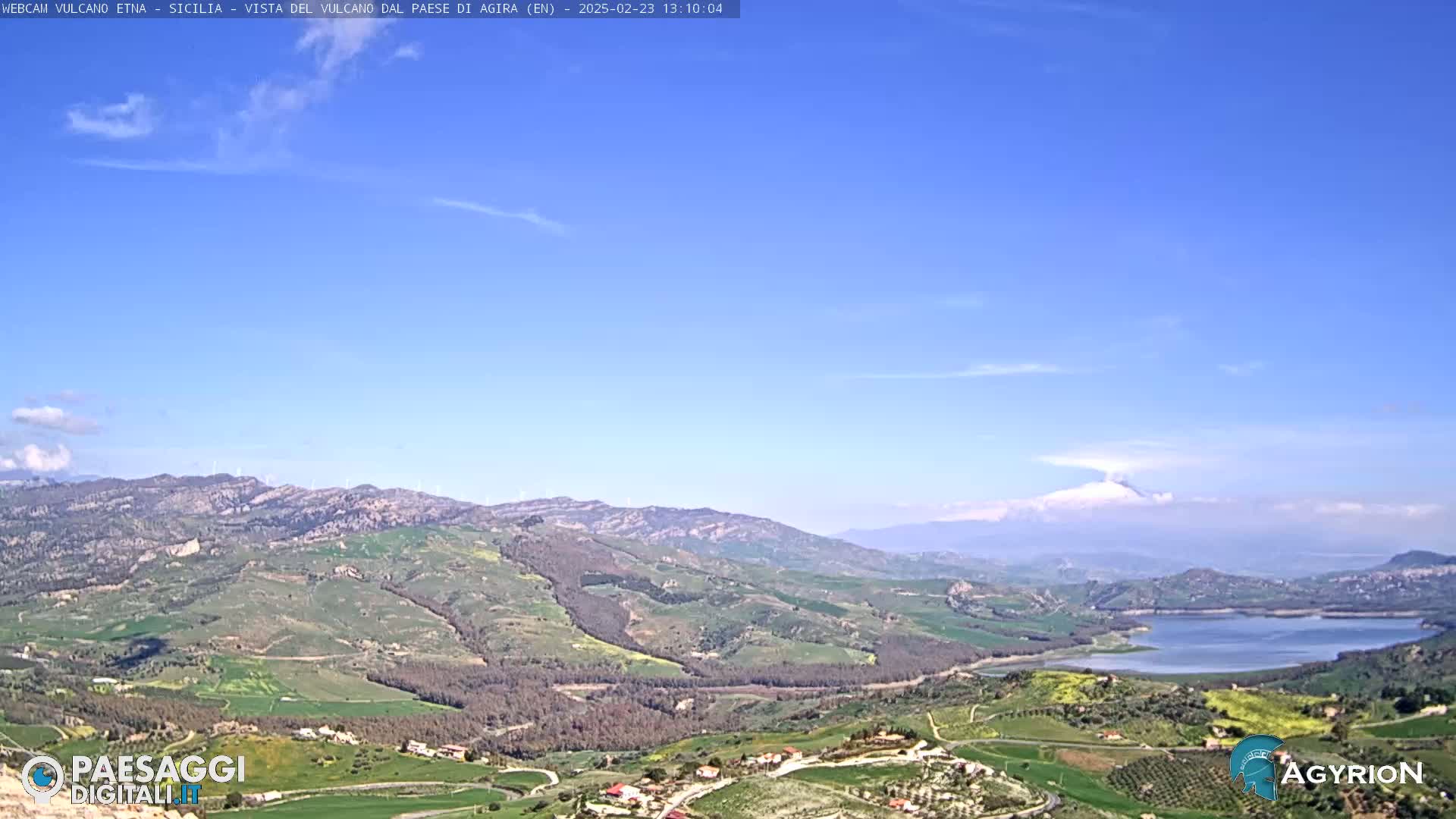 A vast, hilly landscape under a clear blue sky stretches to a distant lake and mountain range.