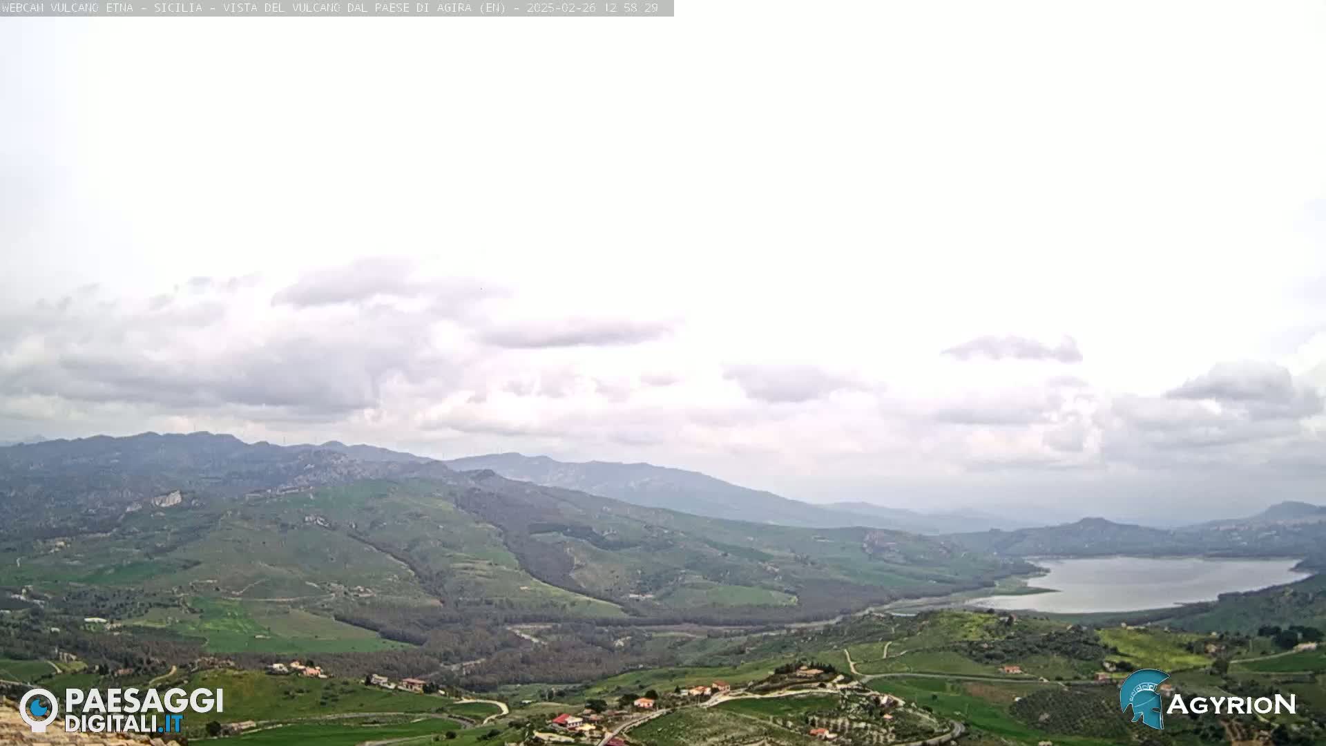 A vast, hilly landscape under a mostly cloudy sky features a lake nestled in a valley.