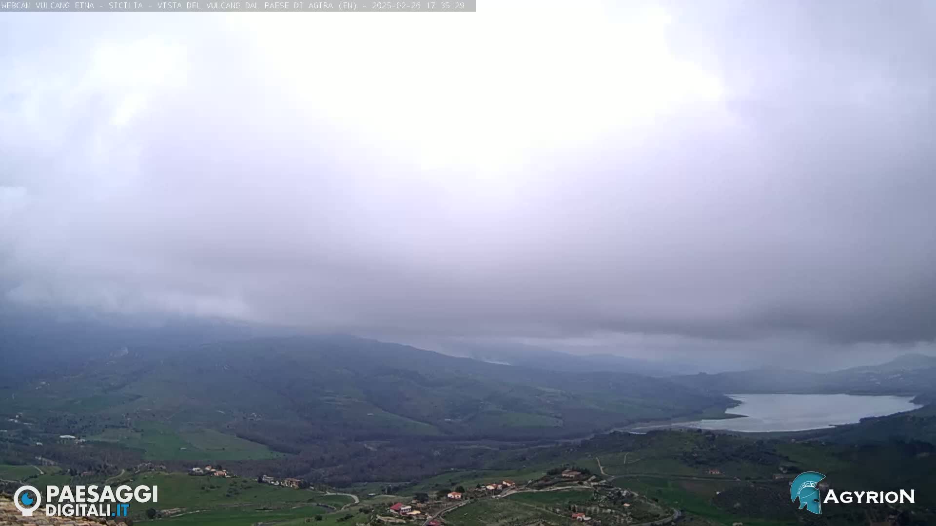 A hilly landscape with a lake is visible under an overcast sky.