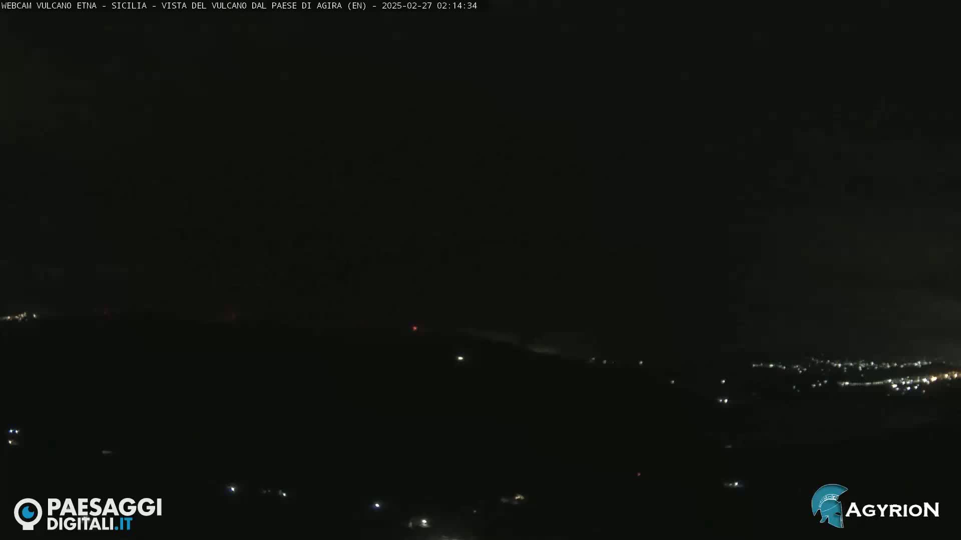 A nighttime, dark view of a hilly landscape with sparsely scattered lights from a distance.