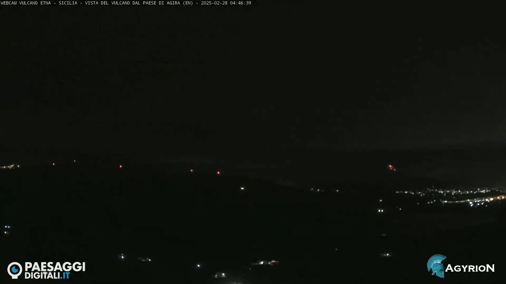 A nighttime long shot of a dark, mountainous landscape sparsely dotted with small lights.