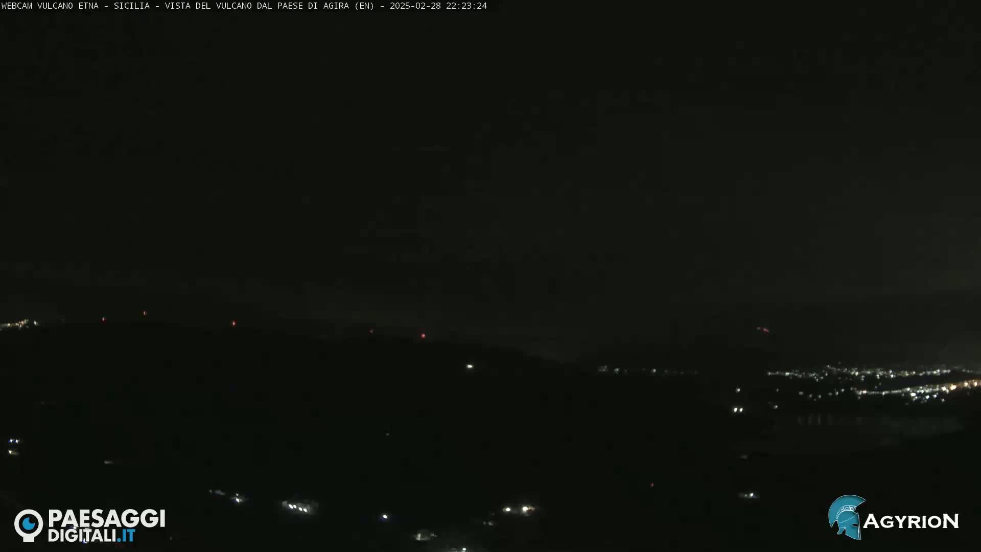 A nighttime long shot shows a dark, hilly landscape with scattered lights from a town below, under a mostly clear sky.