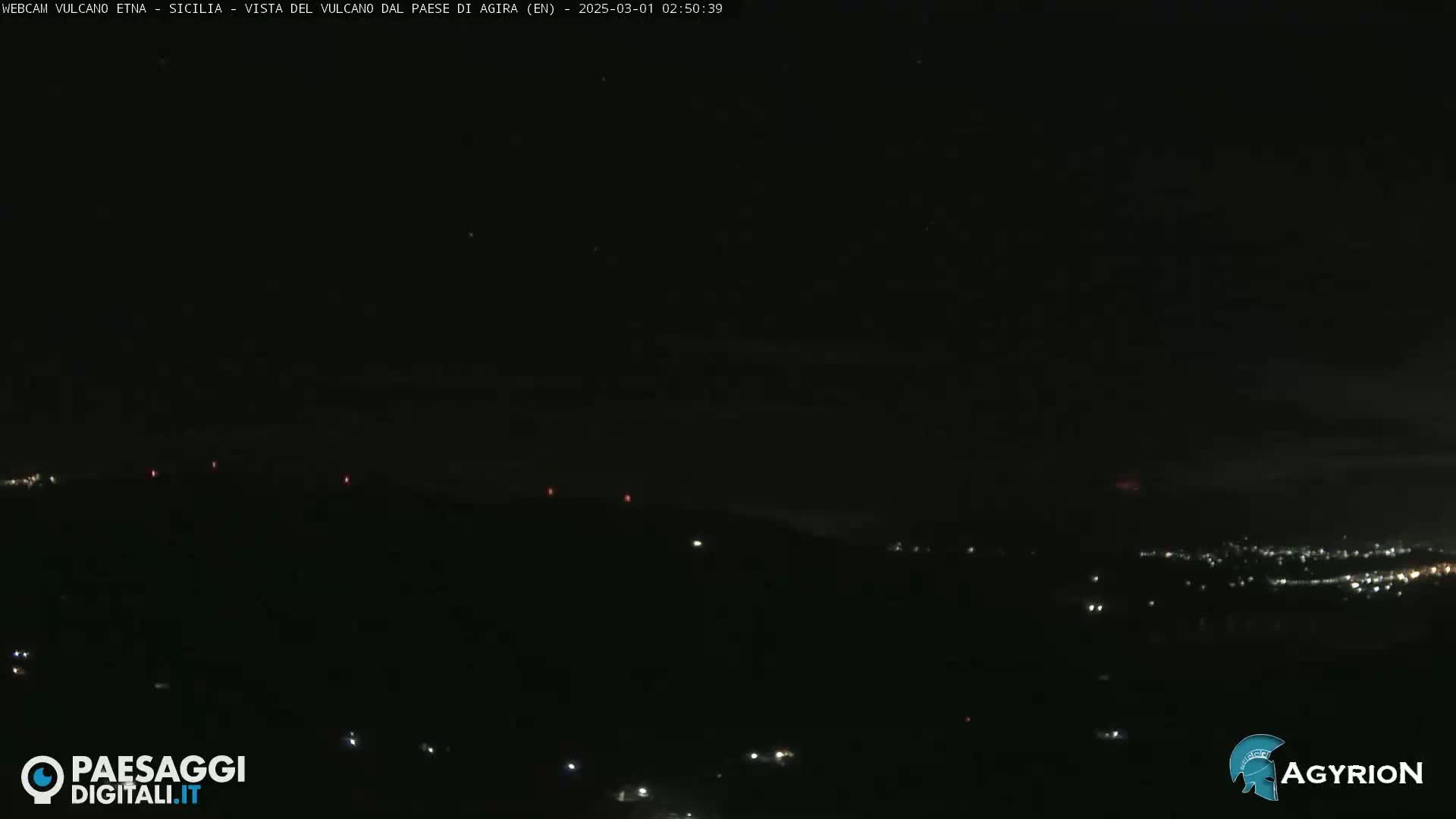 A nighttime long shot shows a dark, hilly landscape with a few scattered lights in the distance under a clear, dark sky.