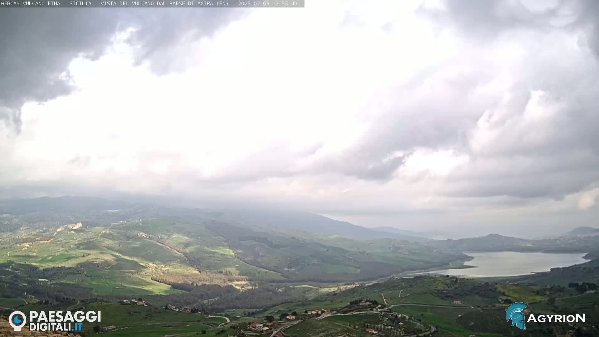 A panoramic view of a hilly landscape with a lake under a mostly cloudy sky.