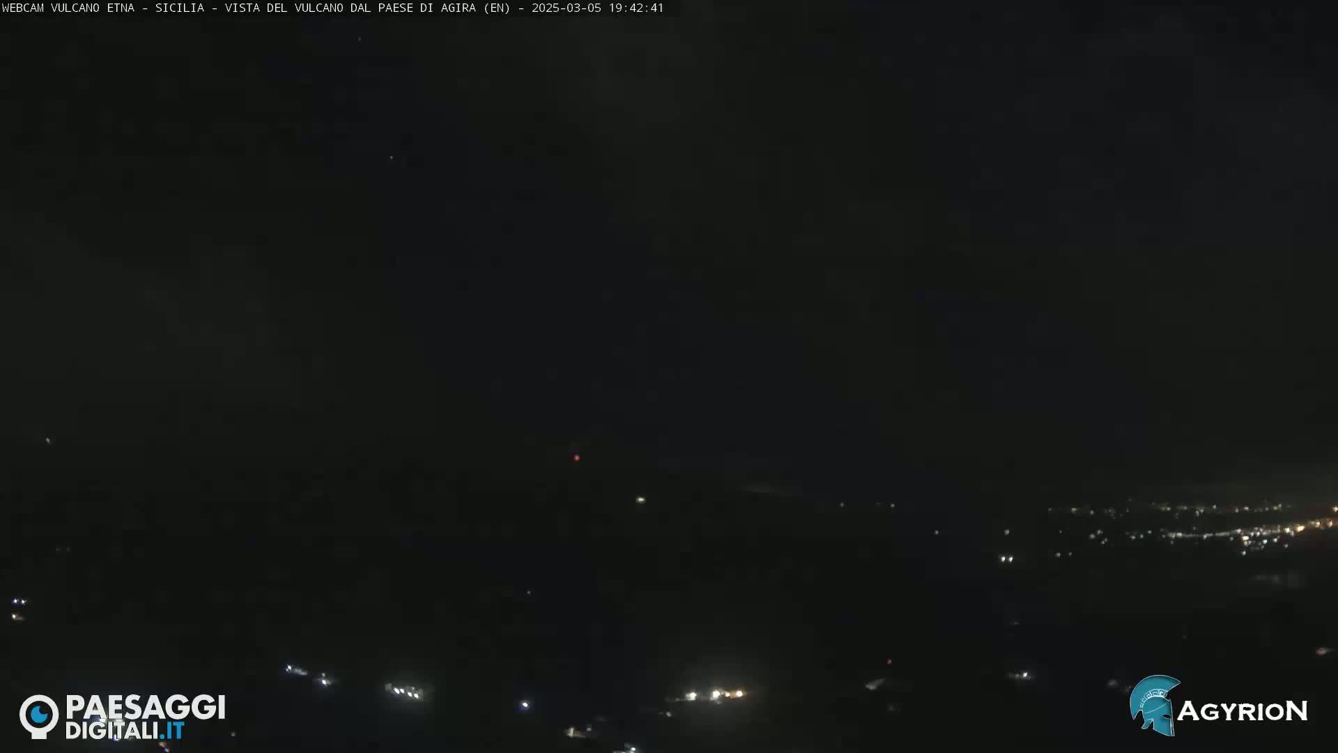 A nighttime long shot shows a dark landscape with a few scattered lights in the distance under a clear, dark sky.