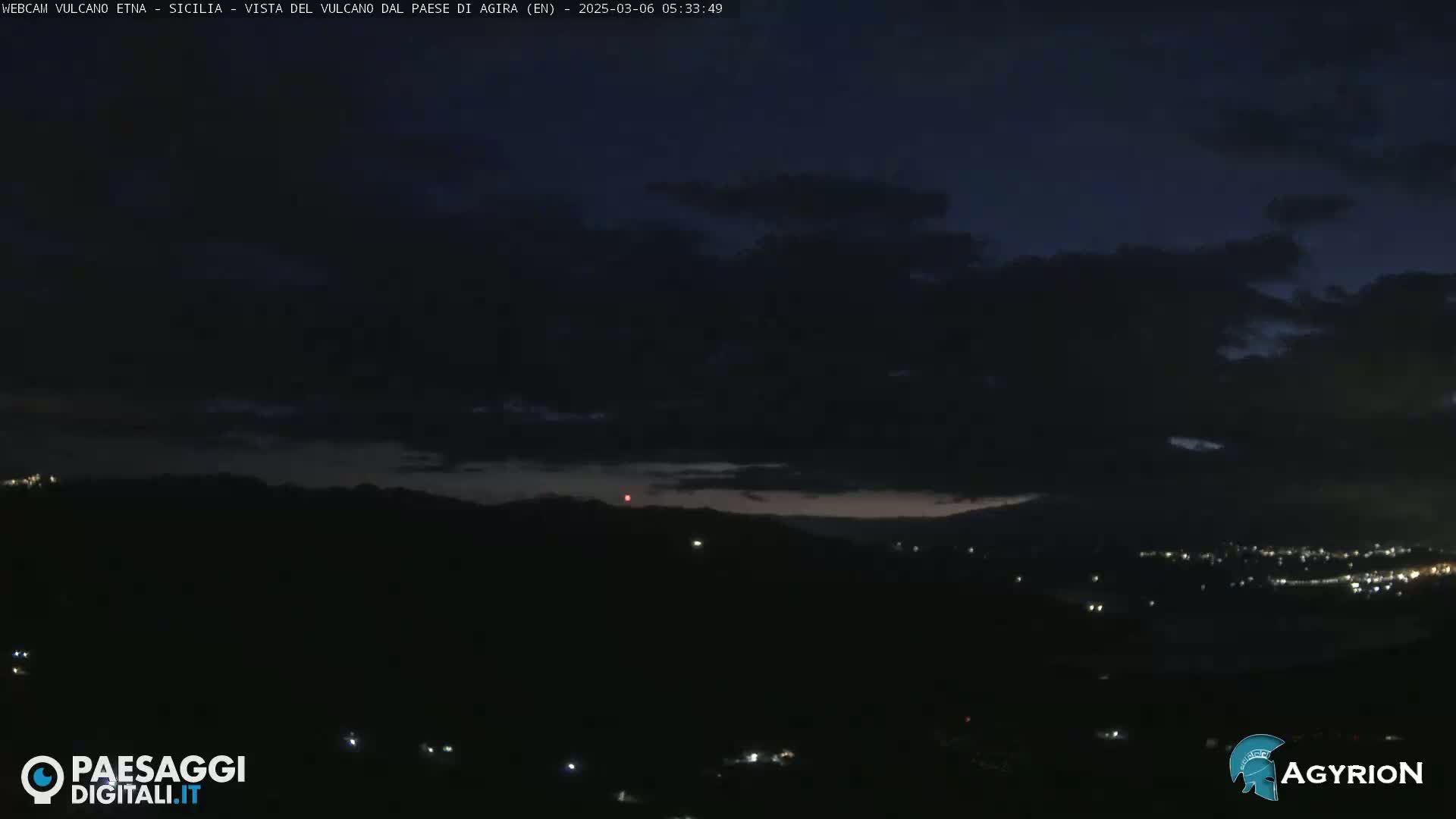 A nighttime, cloudy view shows a dark landscape with distant city lights.