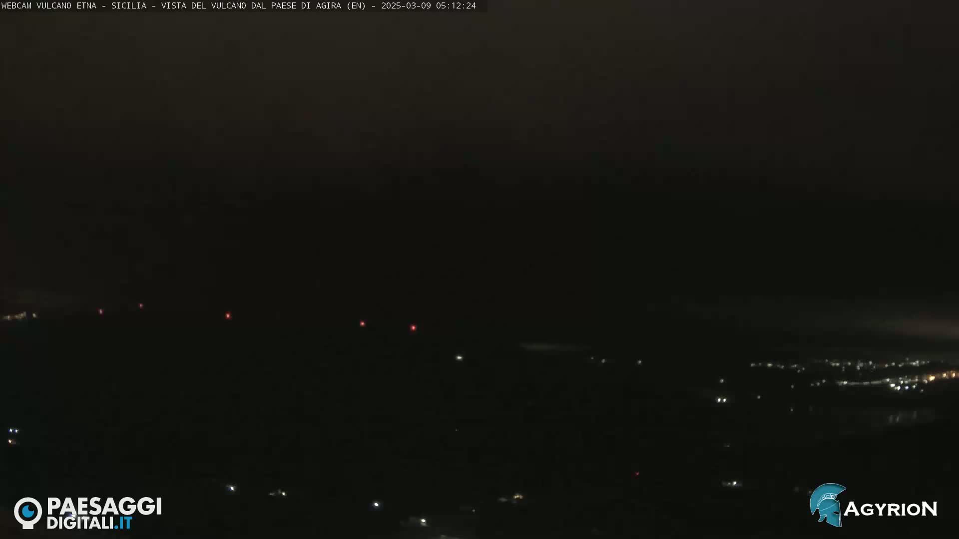A dark, nighttime landscape is visible, with a few scattered lights in the distance.