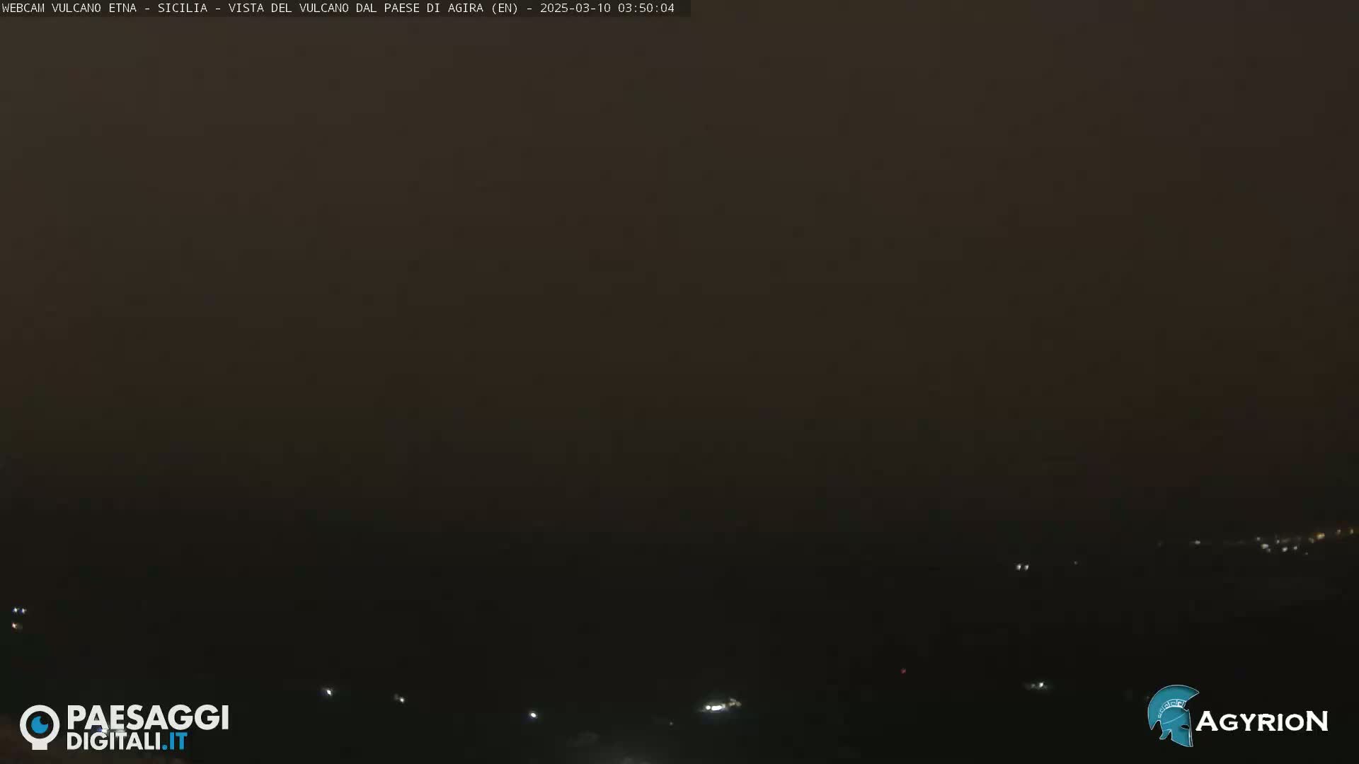 A dark, hazy nighttime landscape is visible, with a few faint lights scattered in the distance.