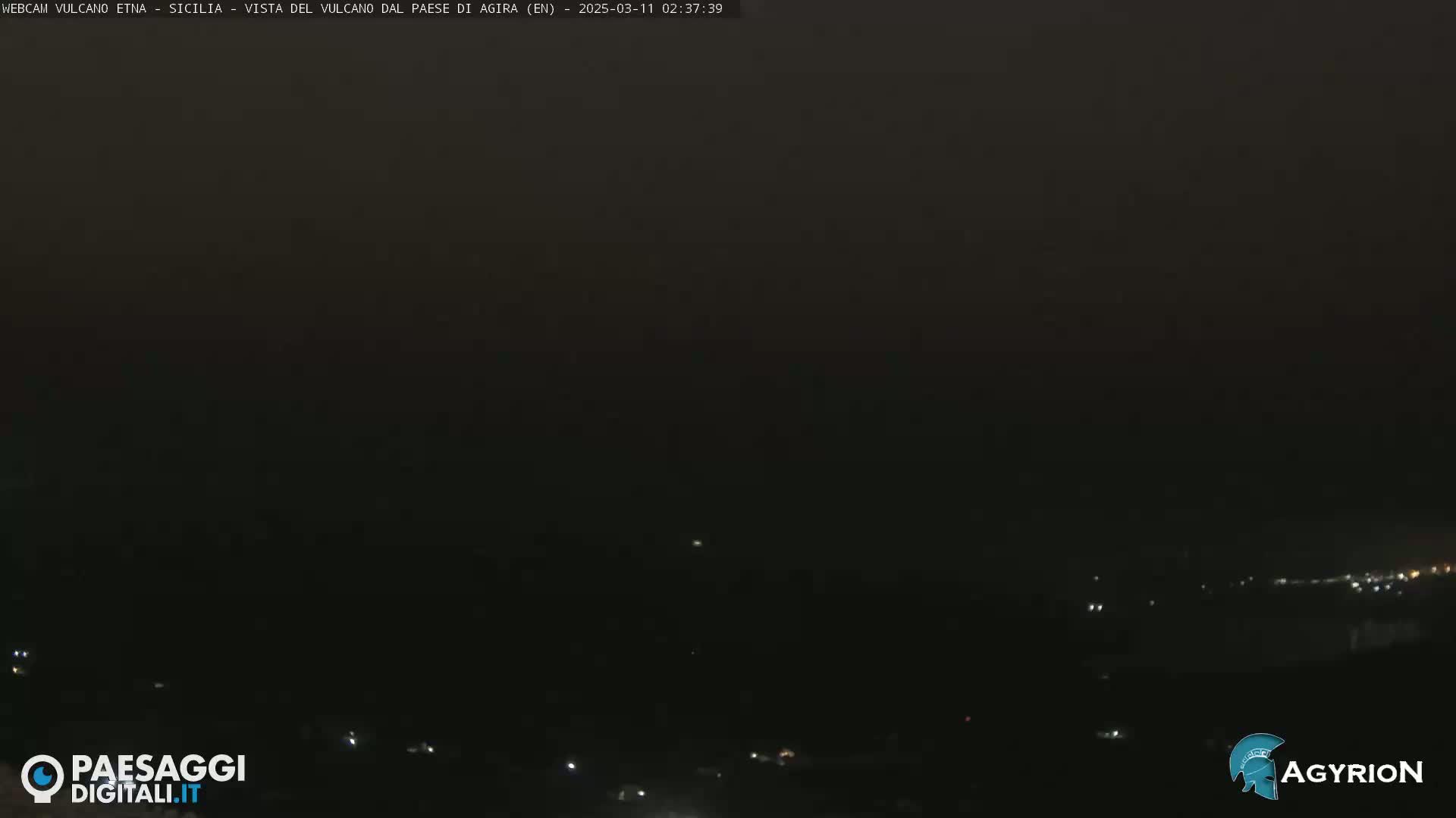 A dark, nighttime landscape is visible, showing a few distant lights and a hazy, dark sky.
