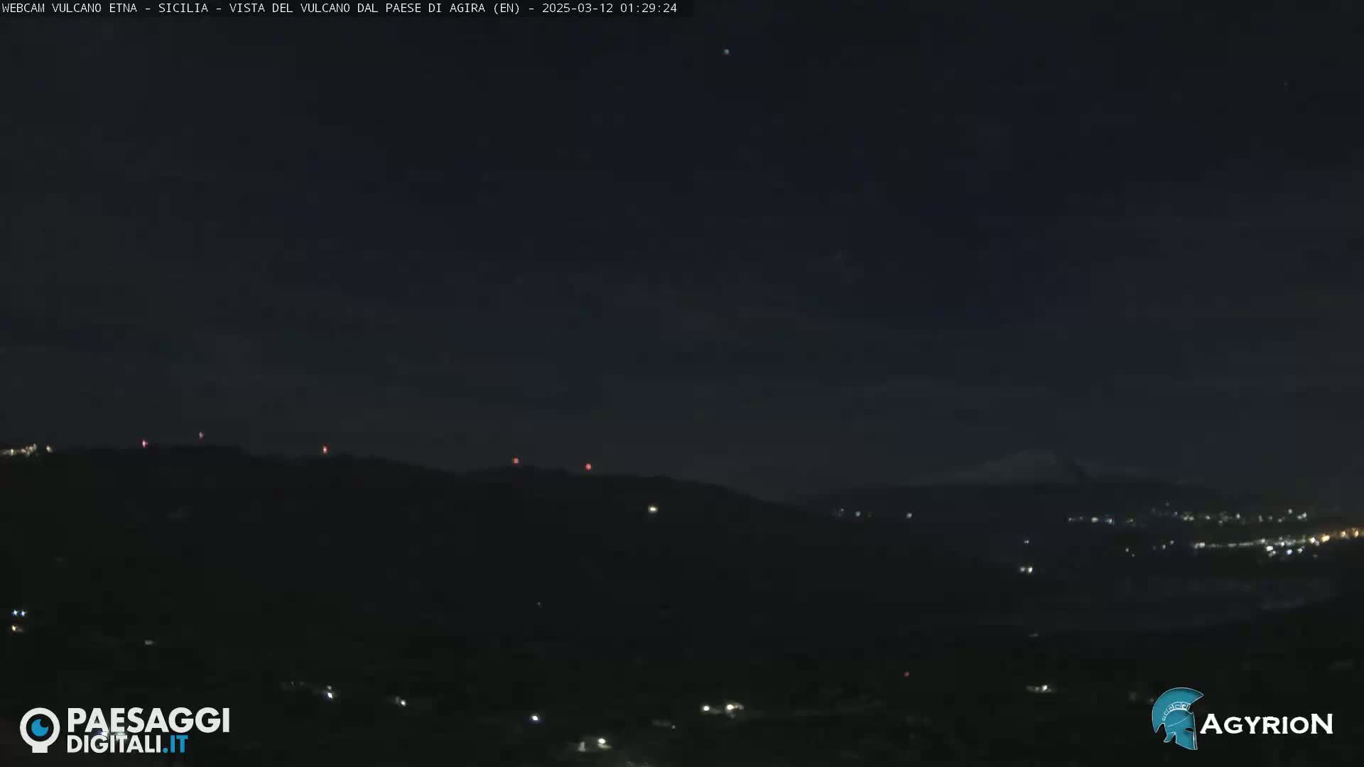 A nighttime long shot shows a dark, hilly landscape with a few scattered lights, under a mostly clear, dark sky.