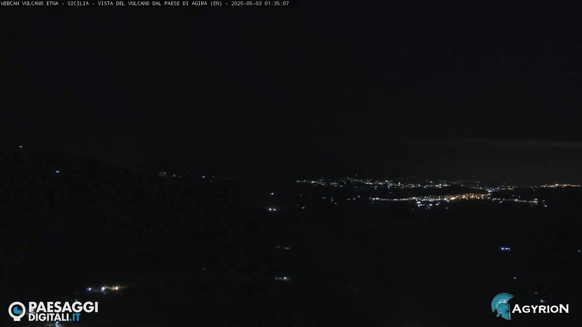A nighttime, long-range view of a city illuminated by scattered lights, set against a dark landscape under a clear sky.