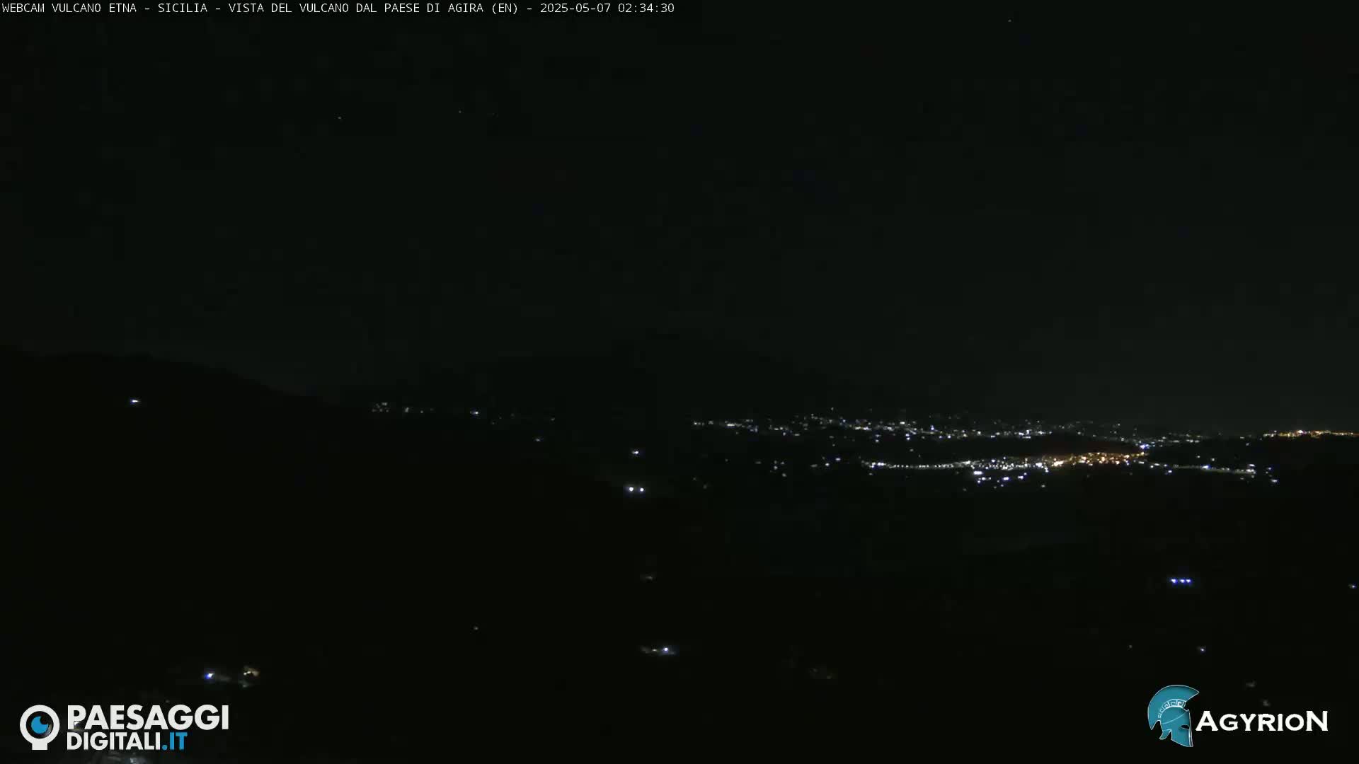 A nighttime view of a city's lights spread across a dark valley, seen from a high vantage point under a clear, starlit sky.