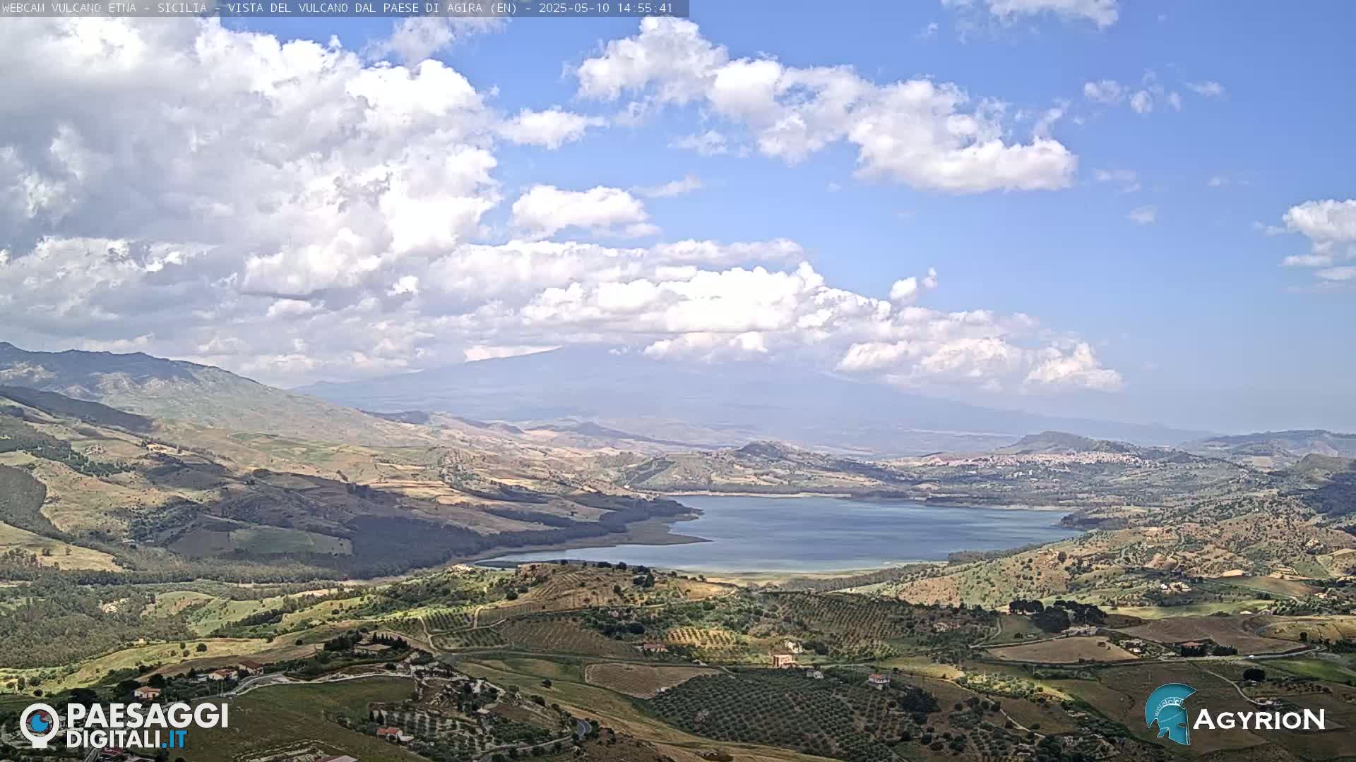 A partly cloudy day reveals a vast, hilly landscape with a large lake nestled in the valley, and mountains in the distance.