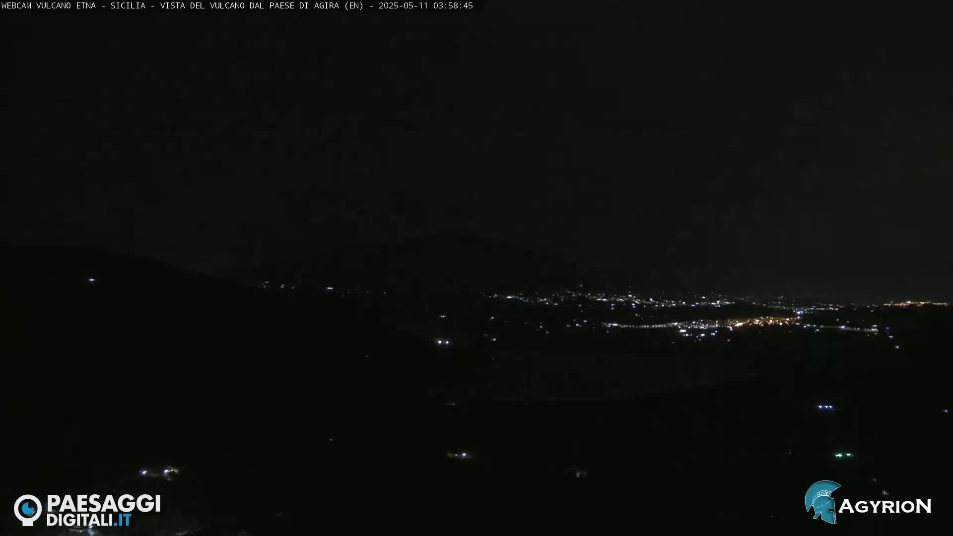 A nighttime view of a distant town's lights illuminated against a dark, clear sky.
