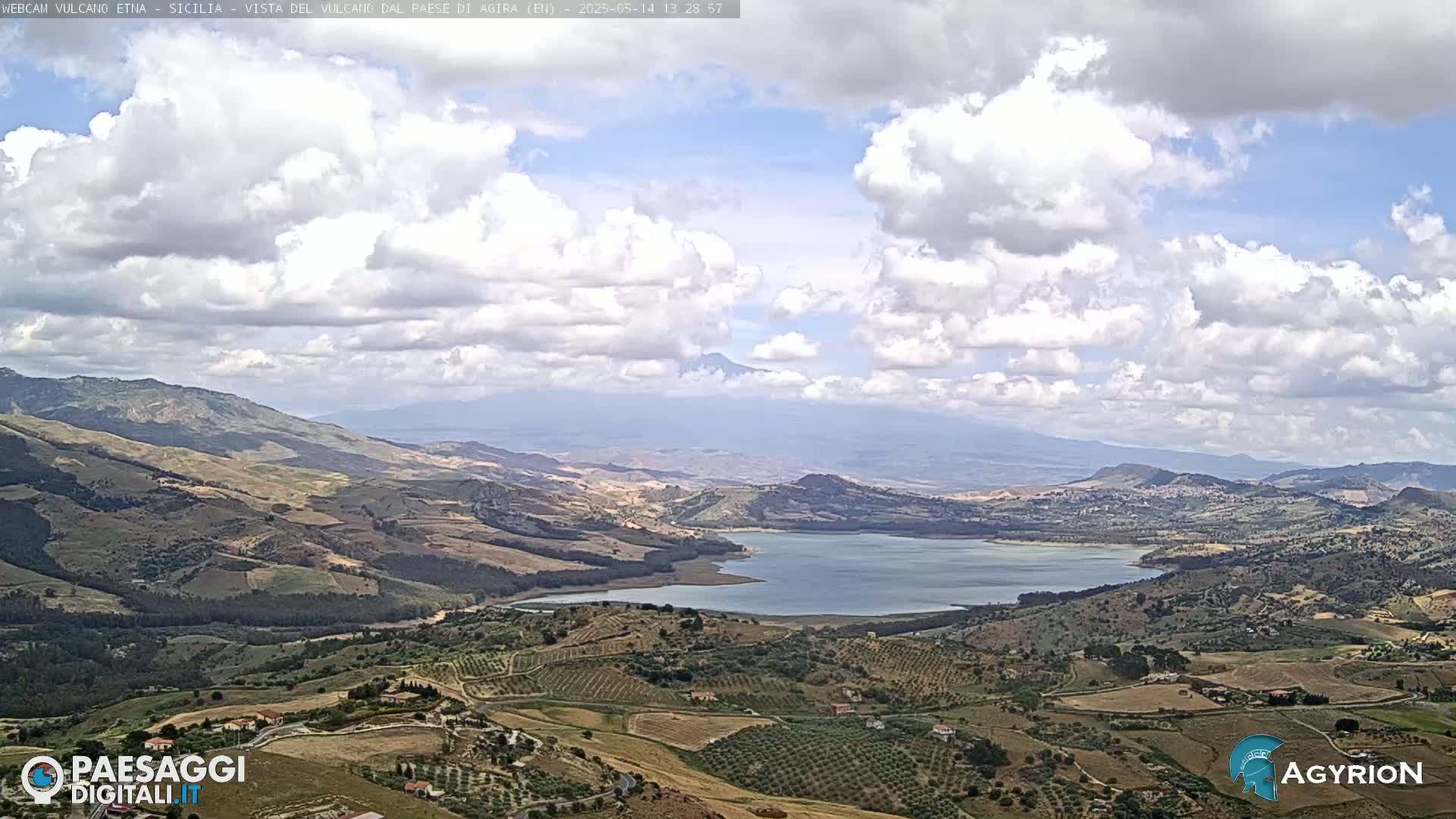 A partly cloudy day reveals a hilly landscape with a large lake,  rolling farmland, and a distant mountain range.