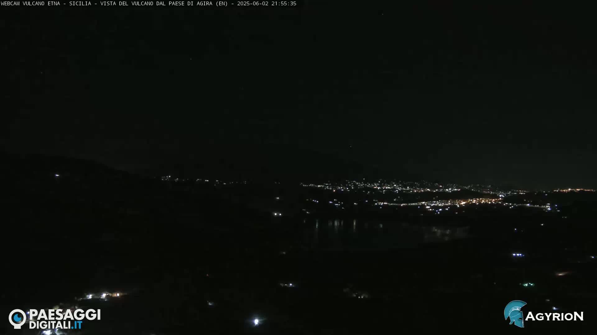 A nighttime, long-range view of a city illuminated by lights, situated below a dark, hilly landscape.