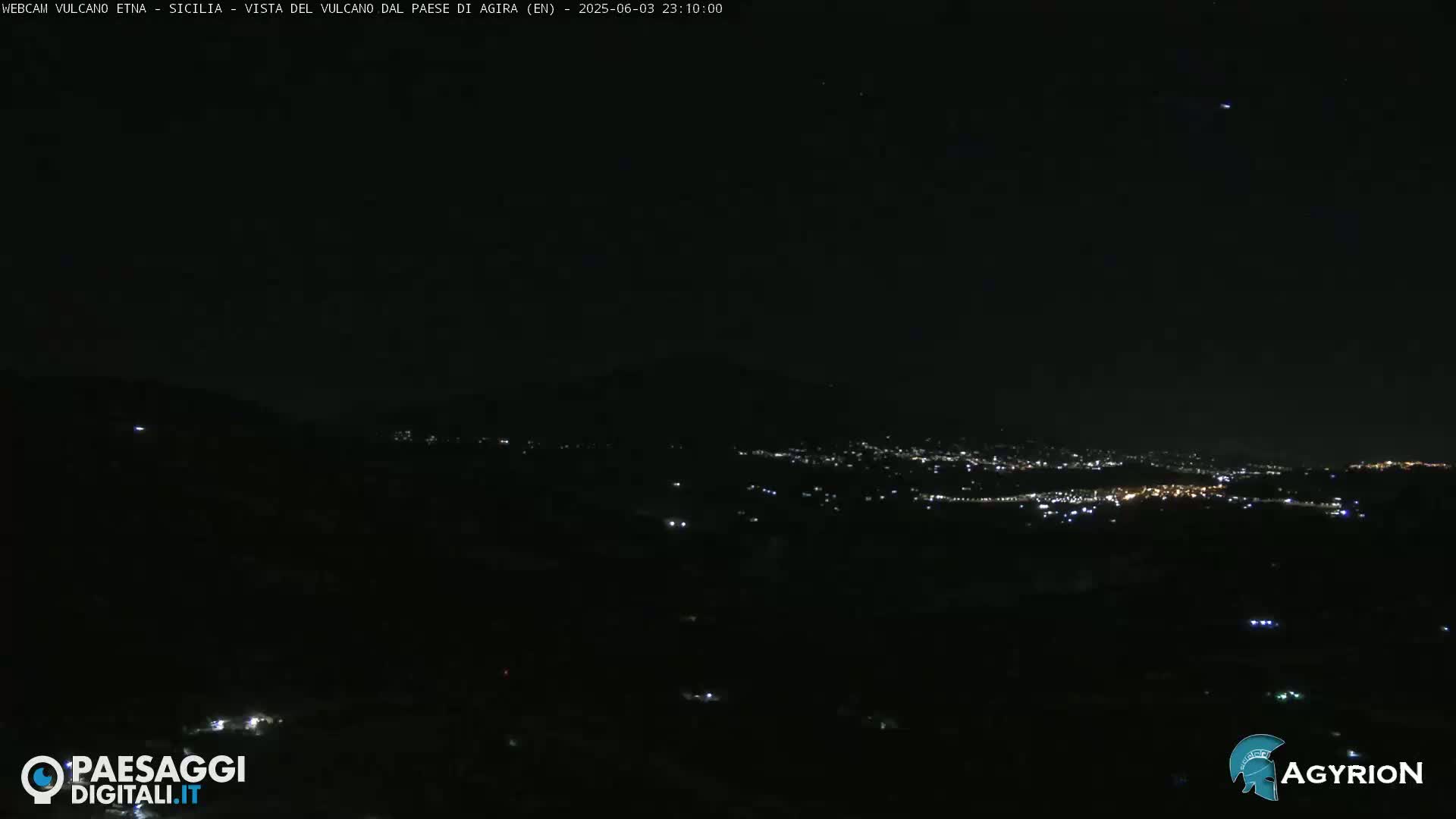 A nighttime long shot shows a dark, hilly landscape with a distant city glowing faintly with lights under a clear, dark sky.