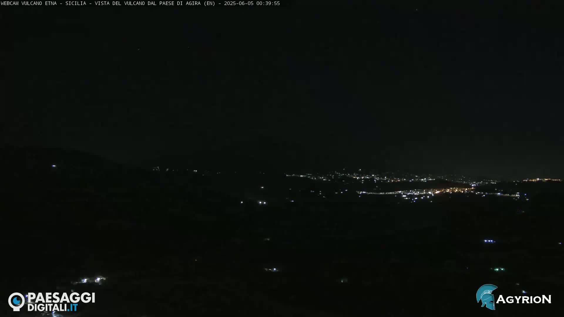 A nighttime long shot shows a dark, distant city illuminated by scattered lights under a clear, dark sky.