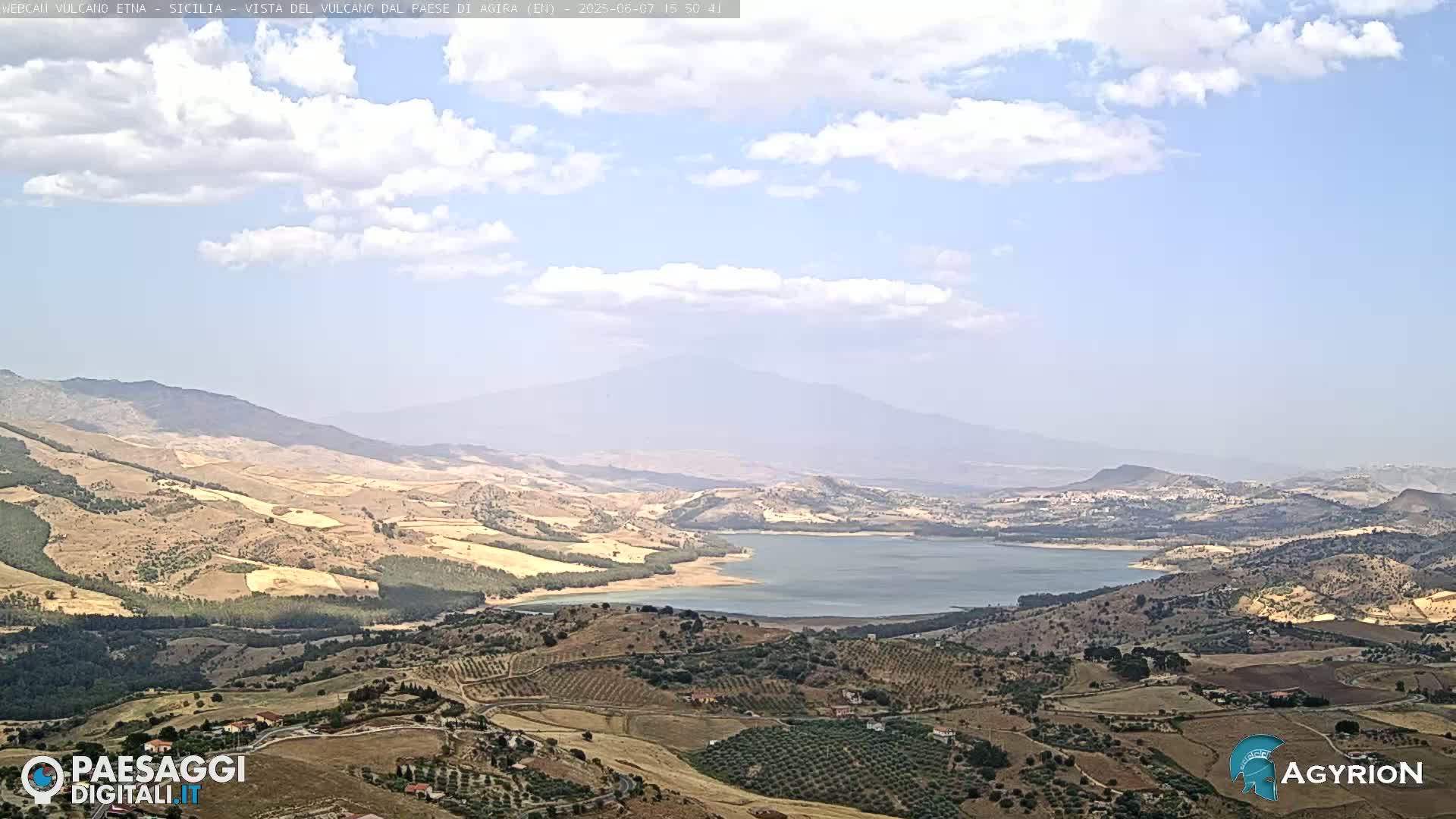 A partly cloudy day reveals a vast, hilly landscape featuring a large lake and a distant, hazy mountain range.