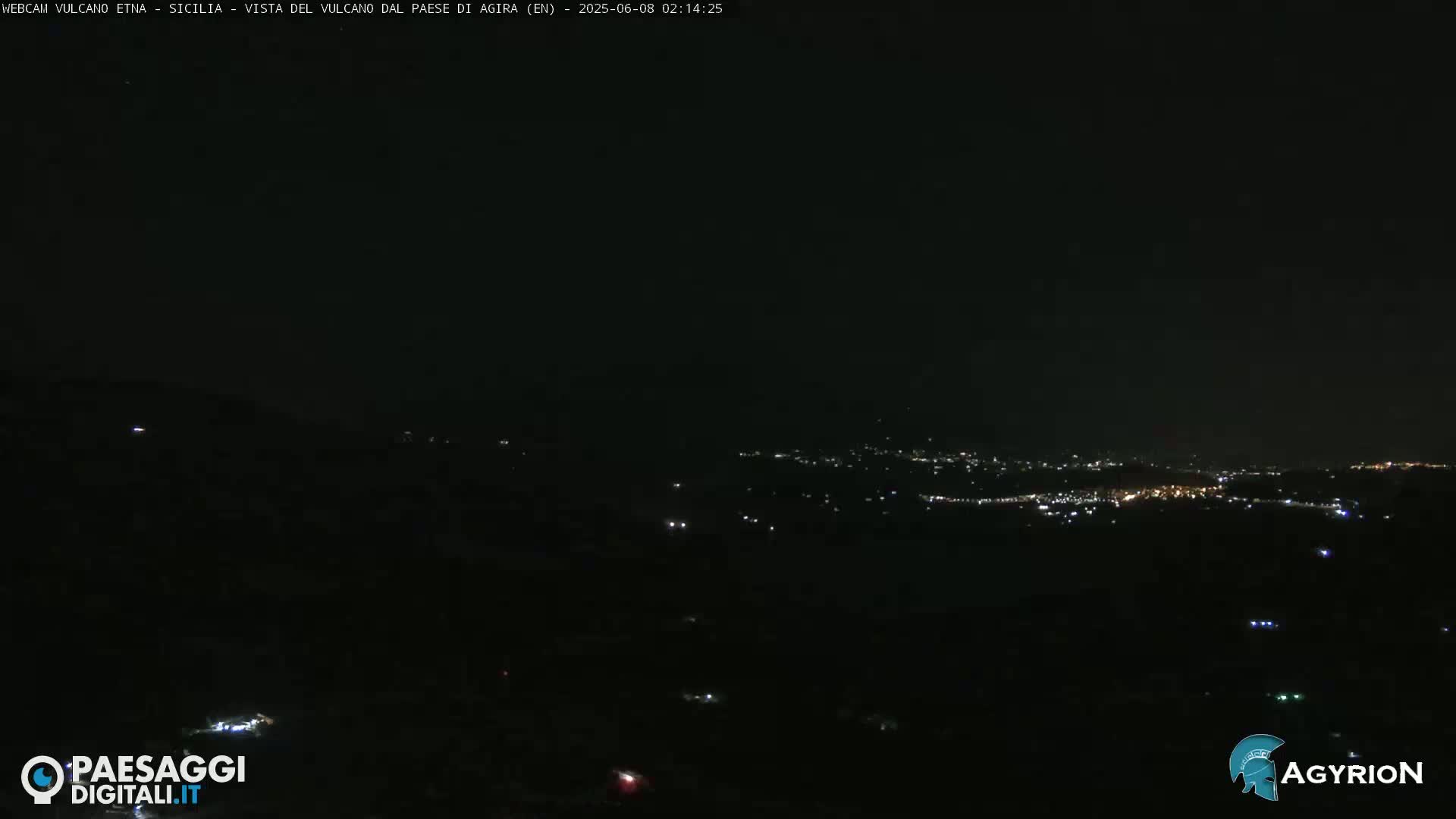 A nighttime long shot of a city's lights spread across a dark landscape under a clear, dark sky.