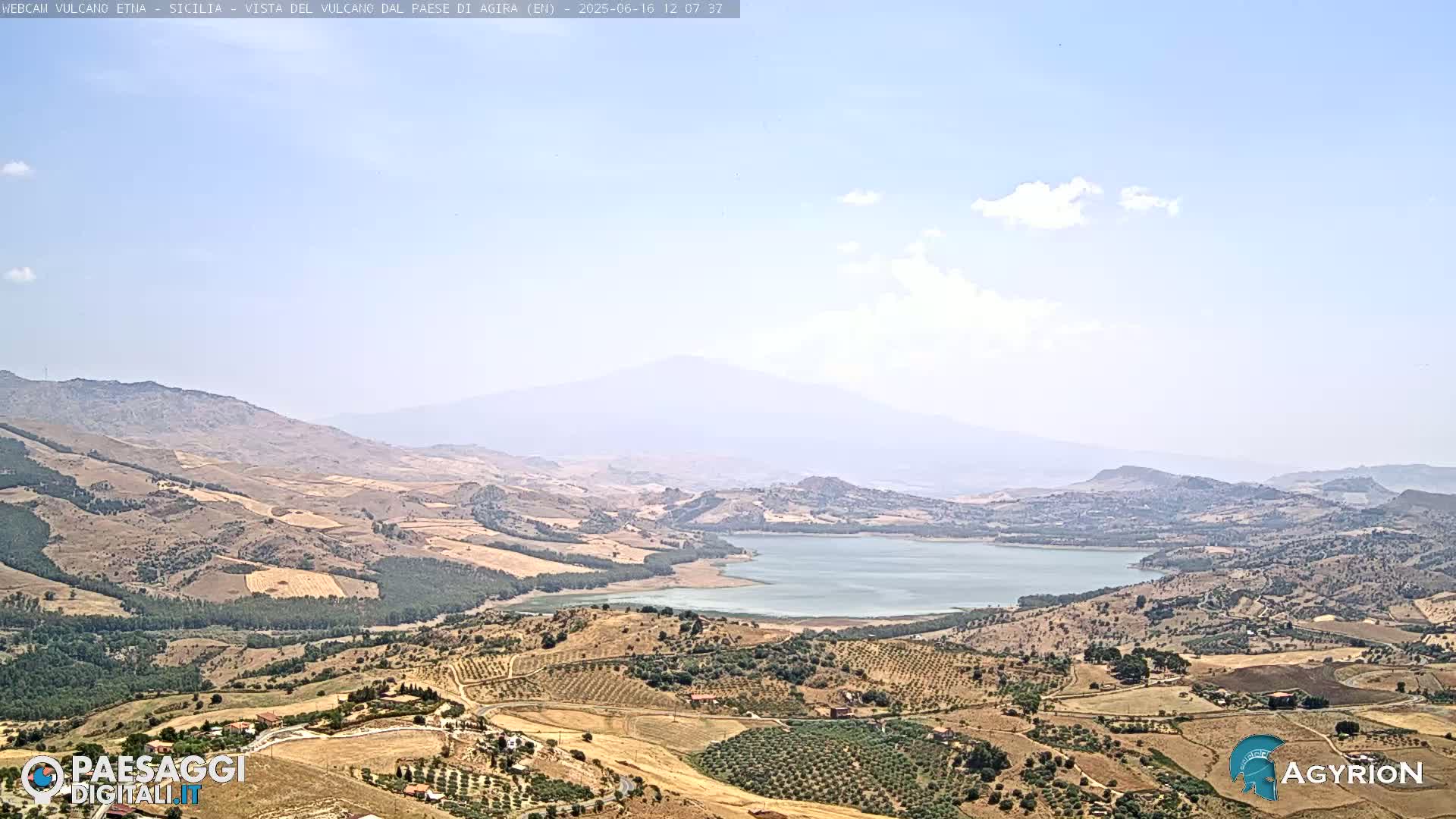 A hazy, sunny day reveals a vast, dry landscape of rolling hills and a lake, with a distant, large mountain in the background.