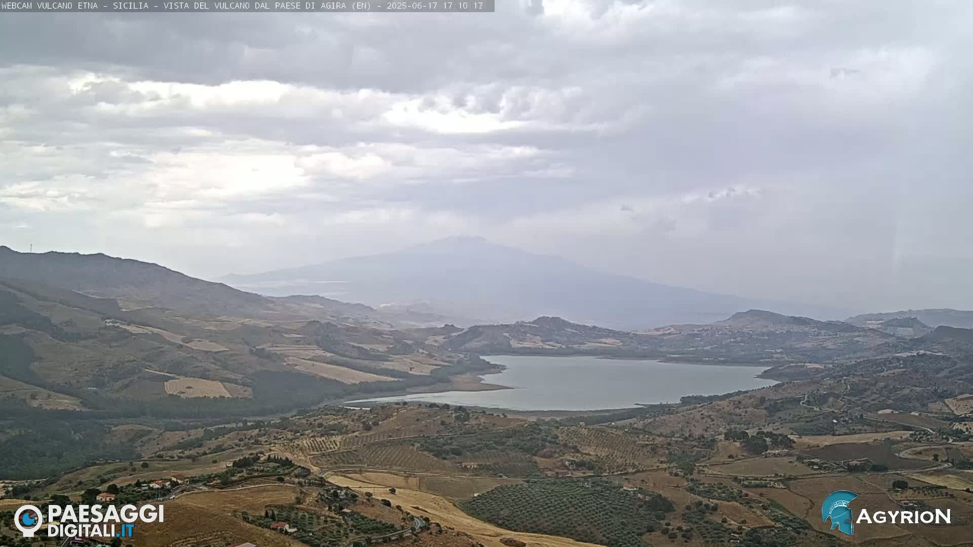 A hazy, overcast day reveals a vast landscape featuring a lake nestled among rolling hills and a distant, large mountain.