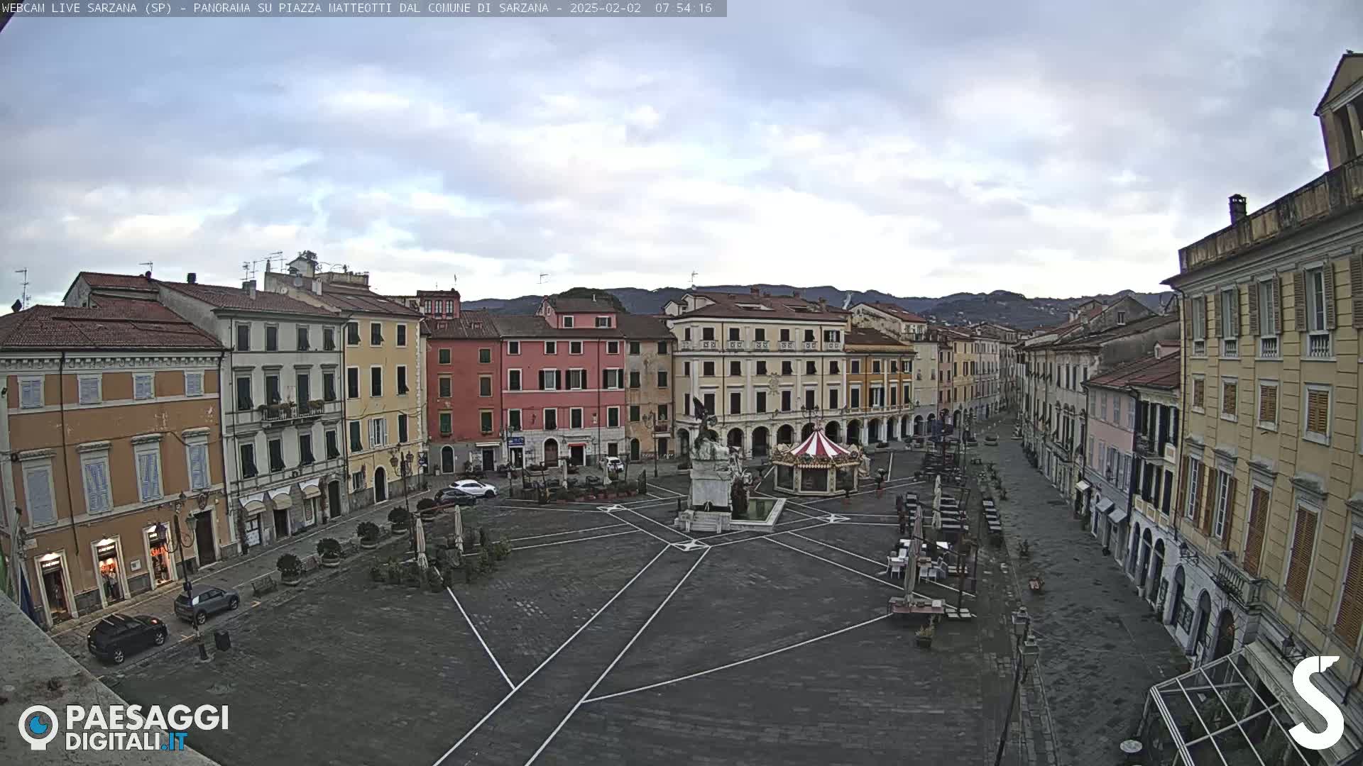 A mostly empty town square with surrounding buildings under a cloudy sky.