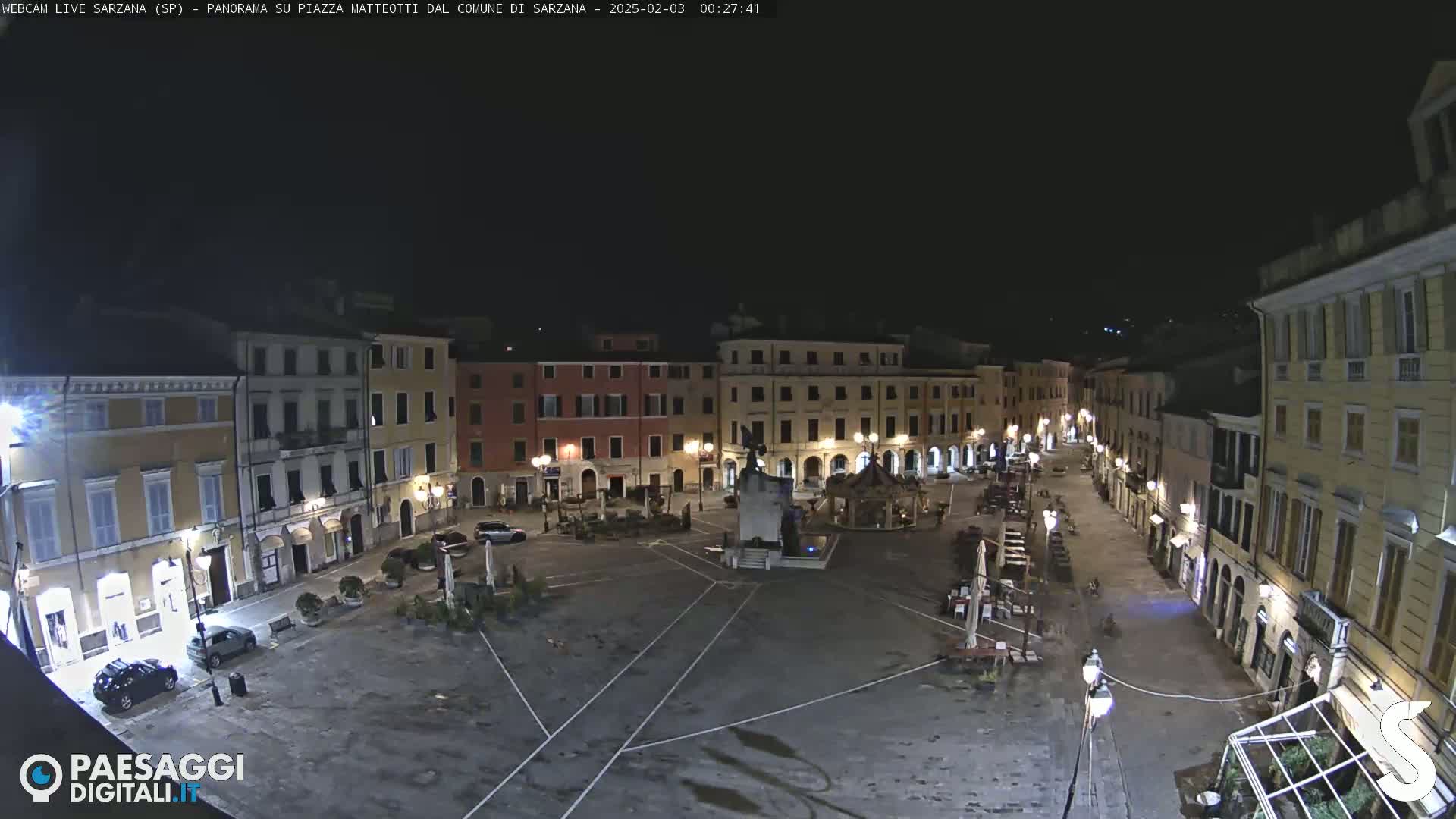 A nighttime view of a mostly empty town square surrounded by illuminated buildings.