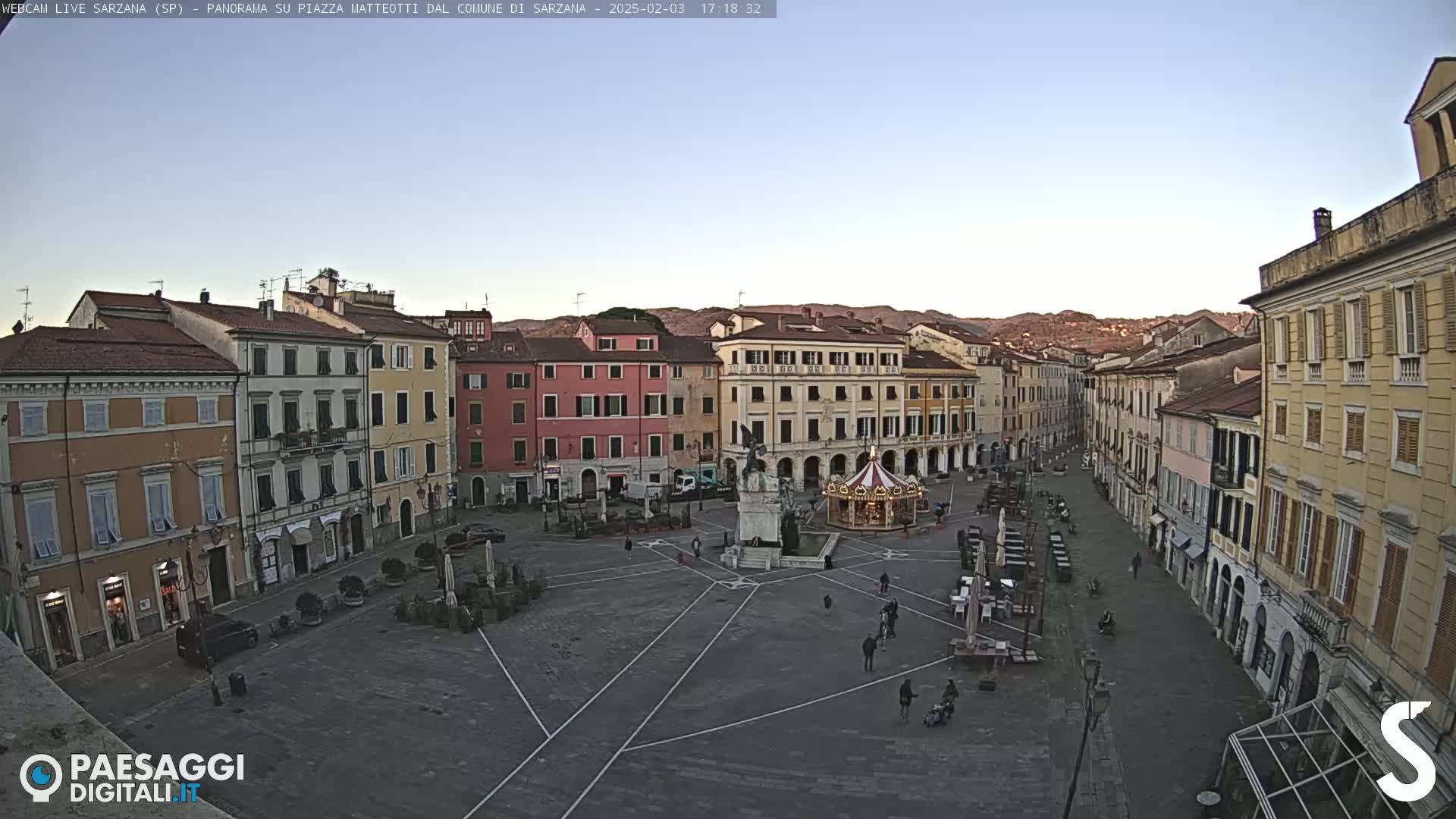 A mostly empty town square, surrounded by multi-story buildings, under a clear twilight sky.