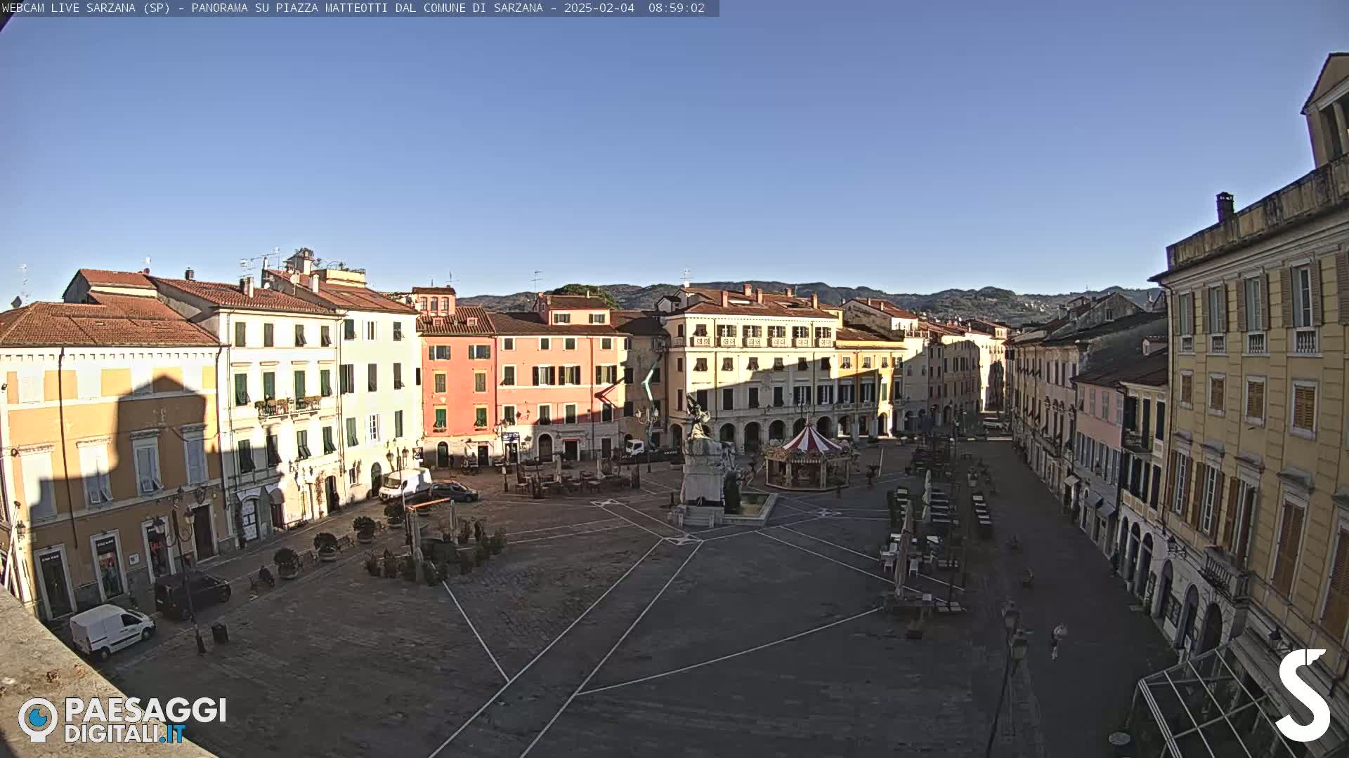A mostly empty town square, surrounded by multi-story buildings, on a sunny day.