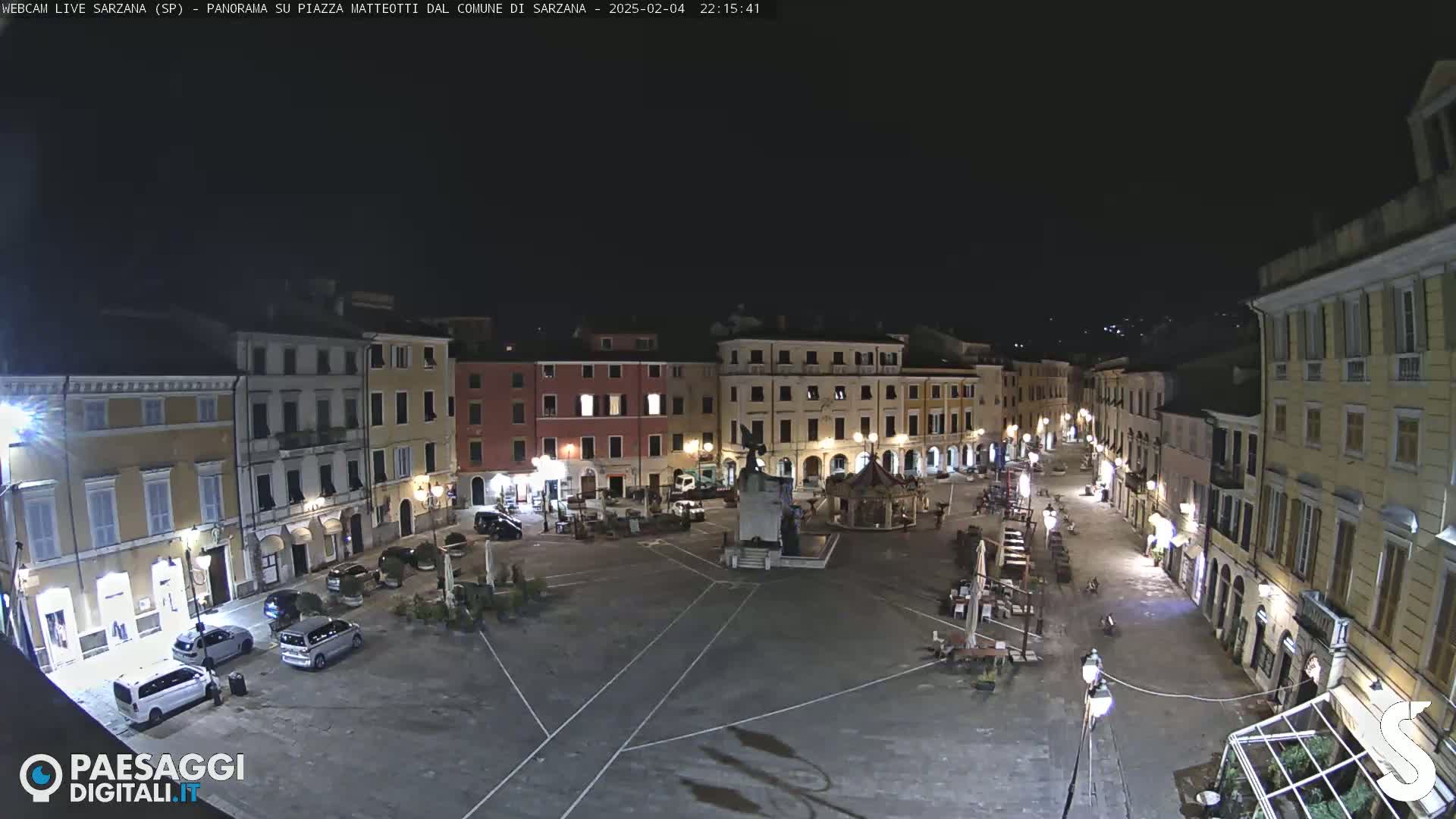 A nighttime view of a mostly empty town square surrounded by illuminated buildings.