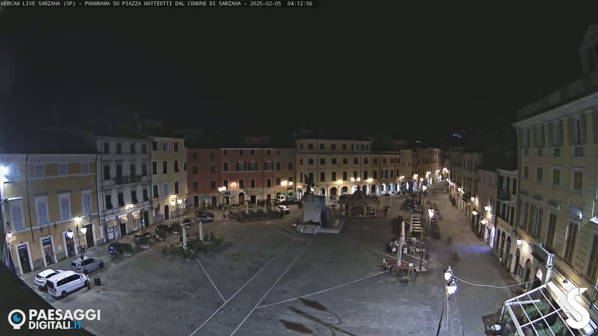 A nighttime, high-angle view of a mostly empty town square surrounded by illuminated buildings.
